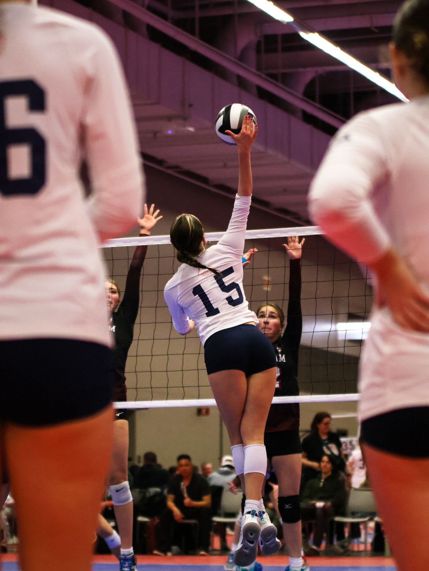 Volleyball player in white jersey jumps high to spike ball during indoor match.