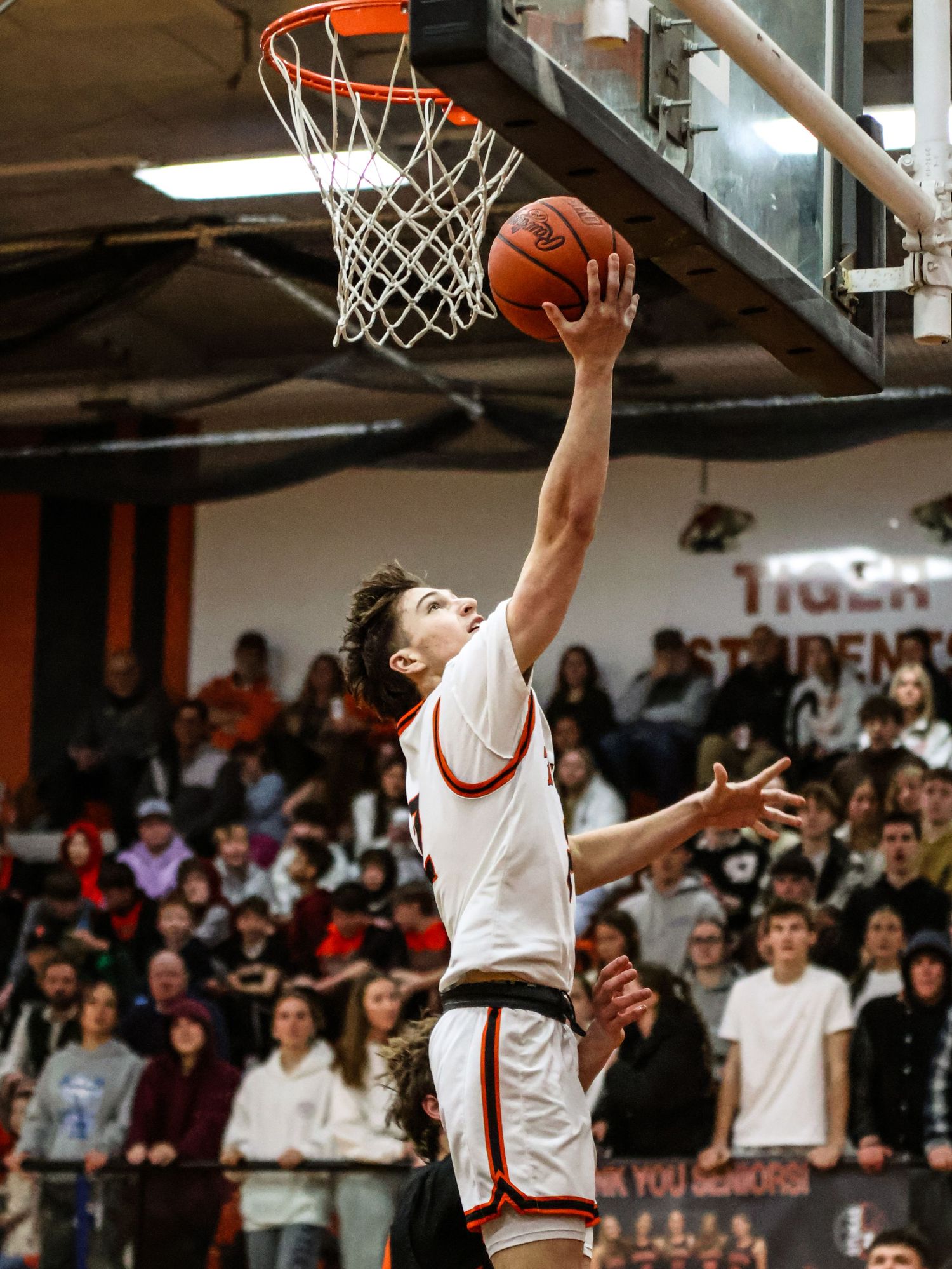 Basketball players leaping for layups during an indoor game with spectators watching.