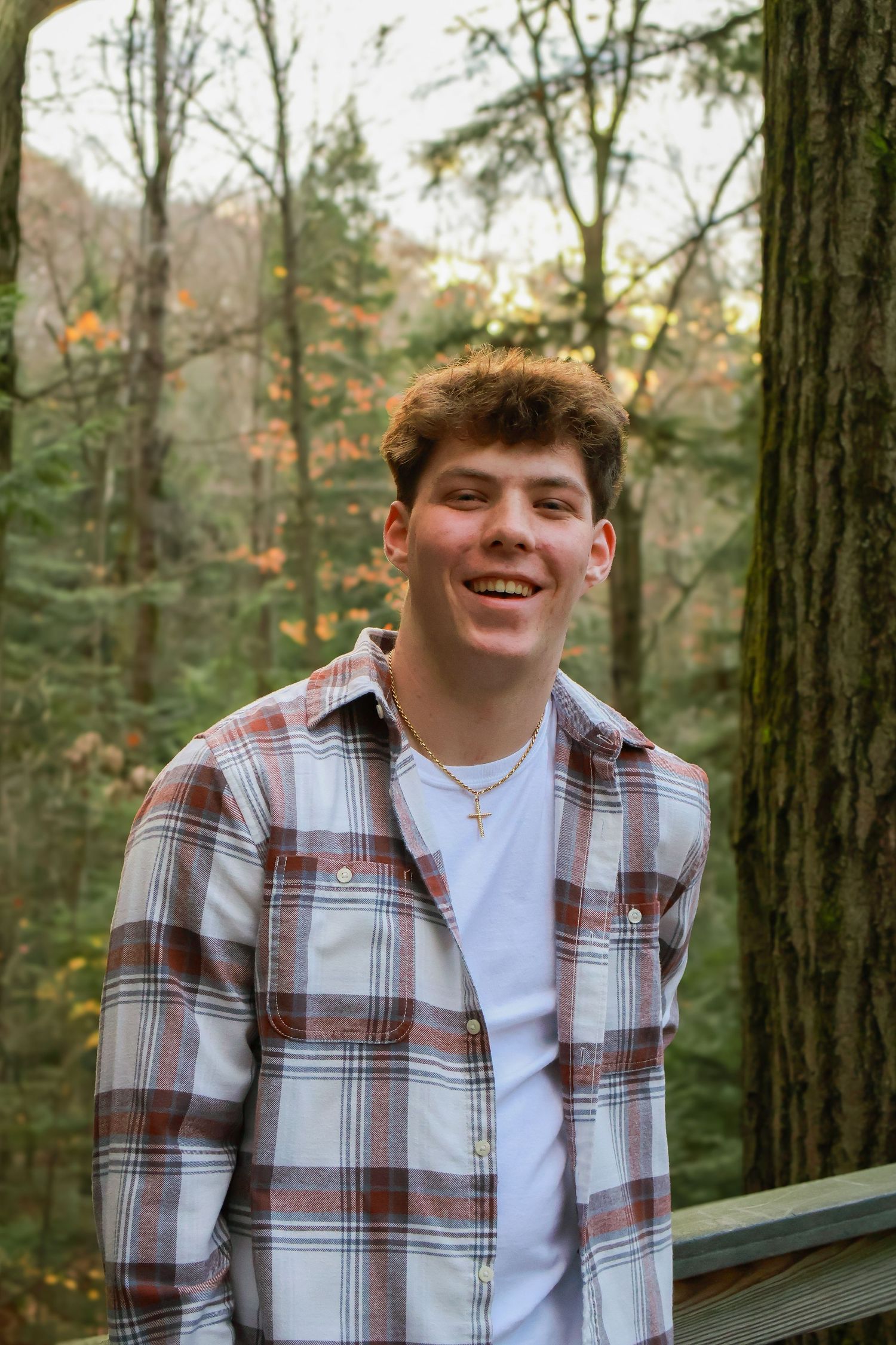 Casual portrait of someone in a plaid flannel shirt and white t-shirt in a forest setting.