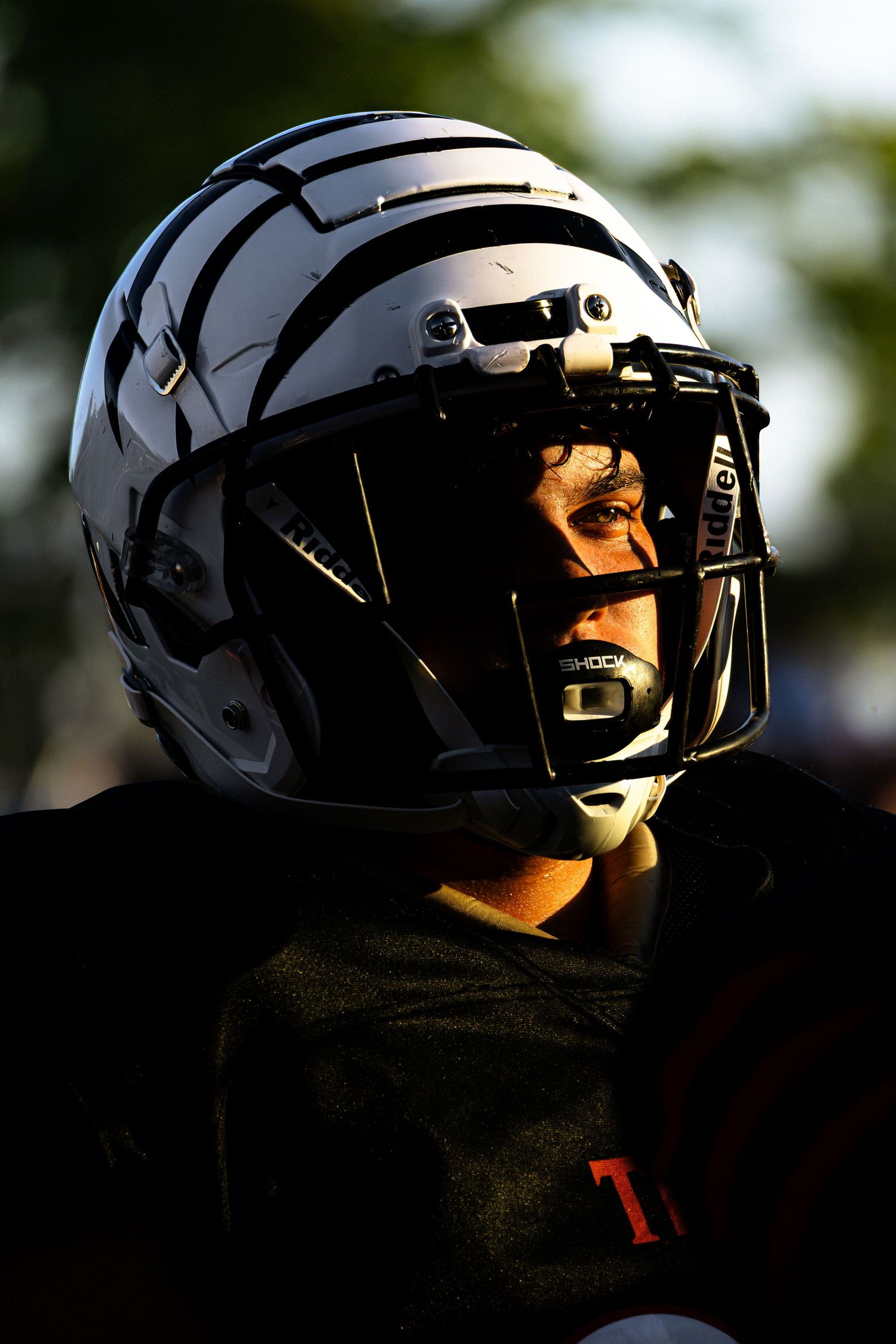 Close-up silhouette of a football player wearing a black helmet with reflective visor in dramatic lighting.