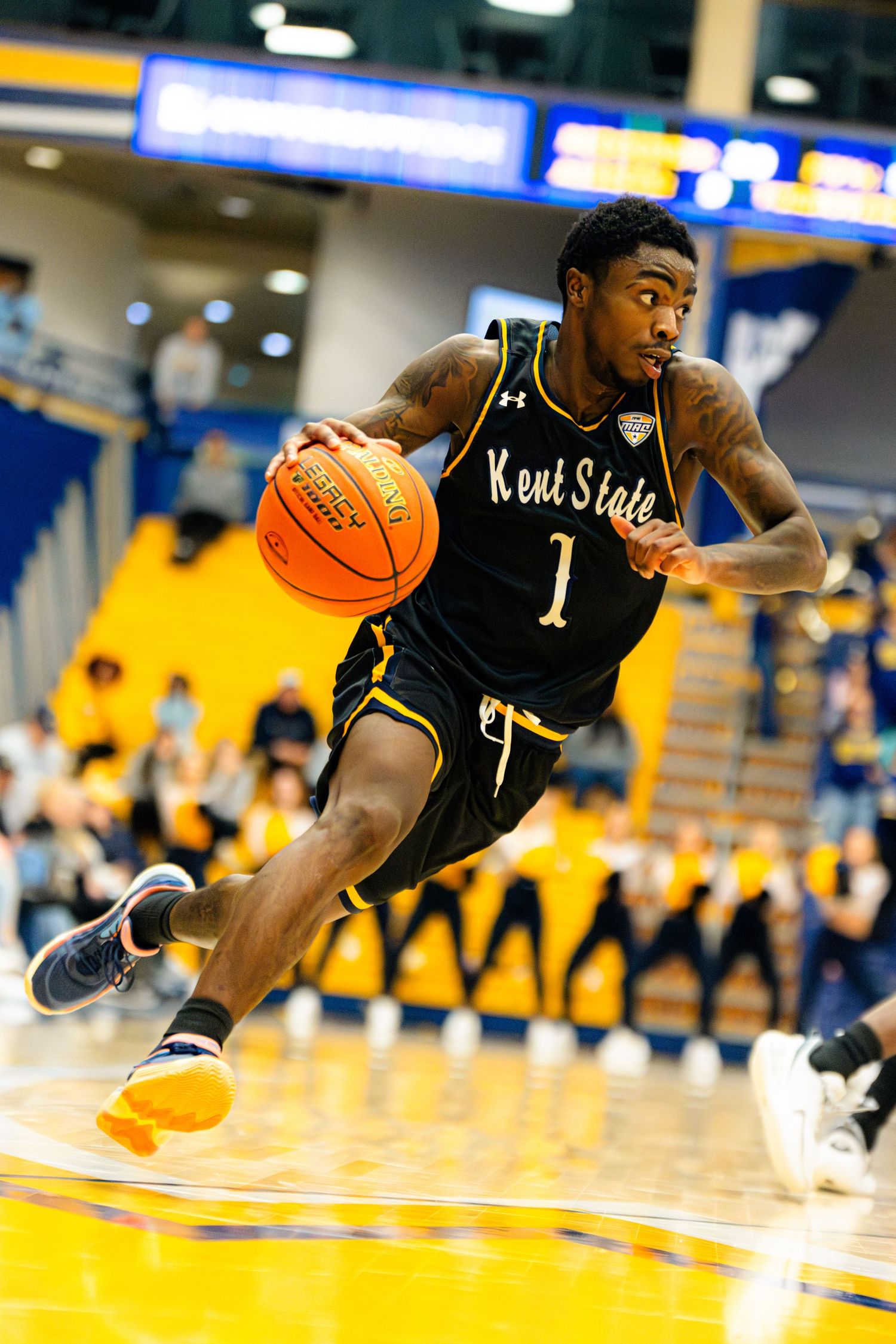 Basketball player in dark jersey dives across court to save ball during intense game action.