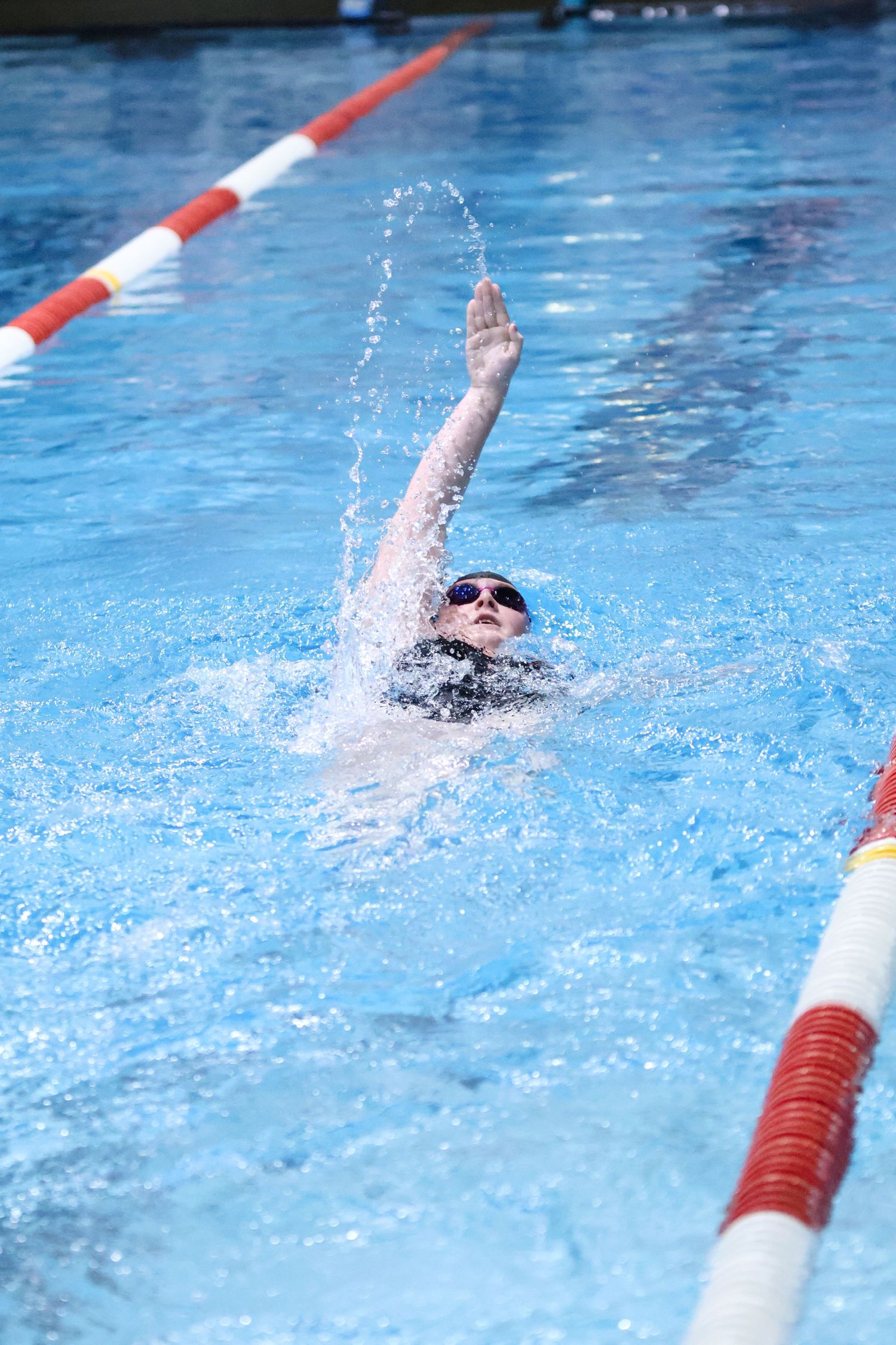 Swimmer doing backstroke in pool with water splashing during competition.