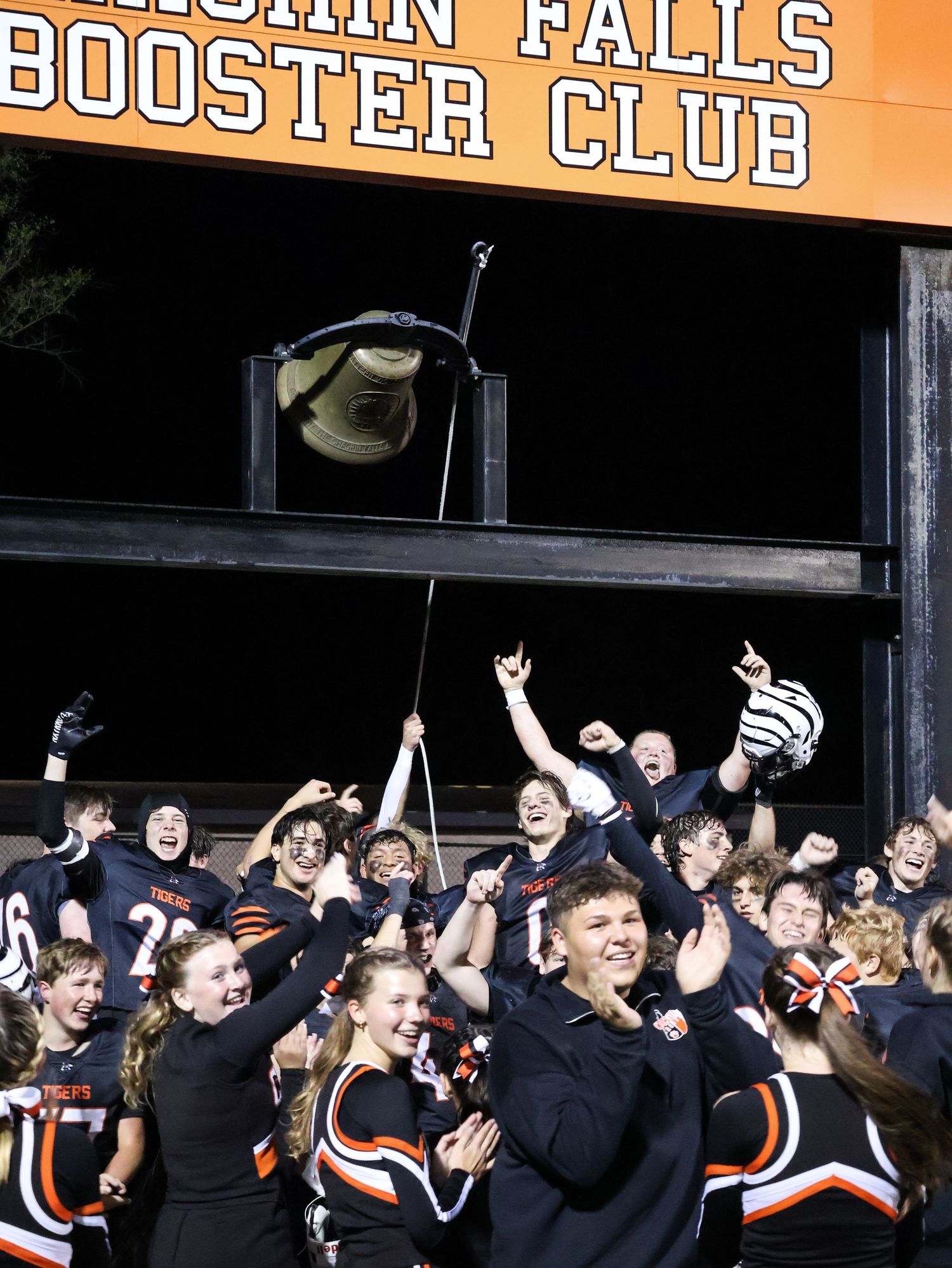 Excited crowd of students in black and orange uniforms cheer under Booster Club sign.
