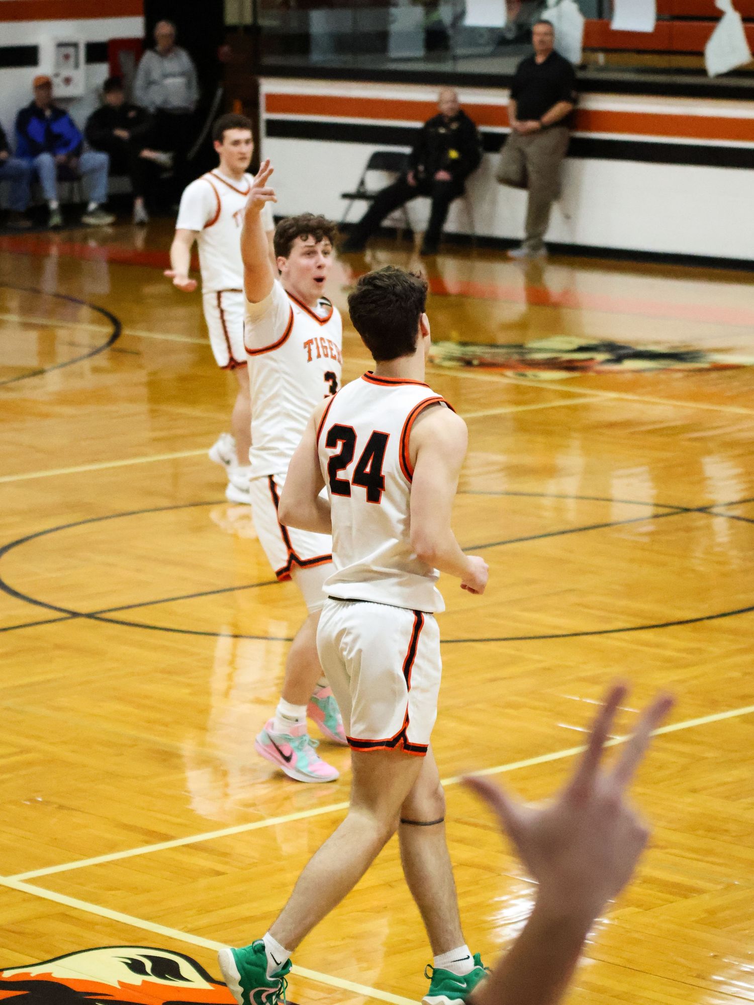 Basketball players in white jerseys moving across a wooden court during a game.