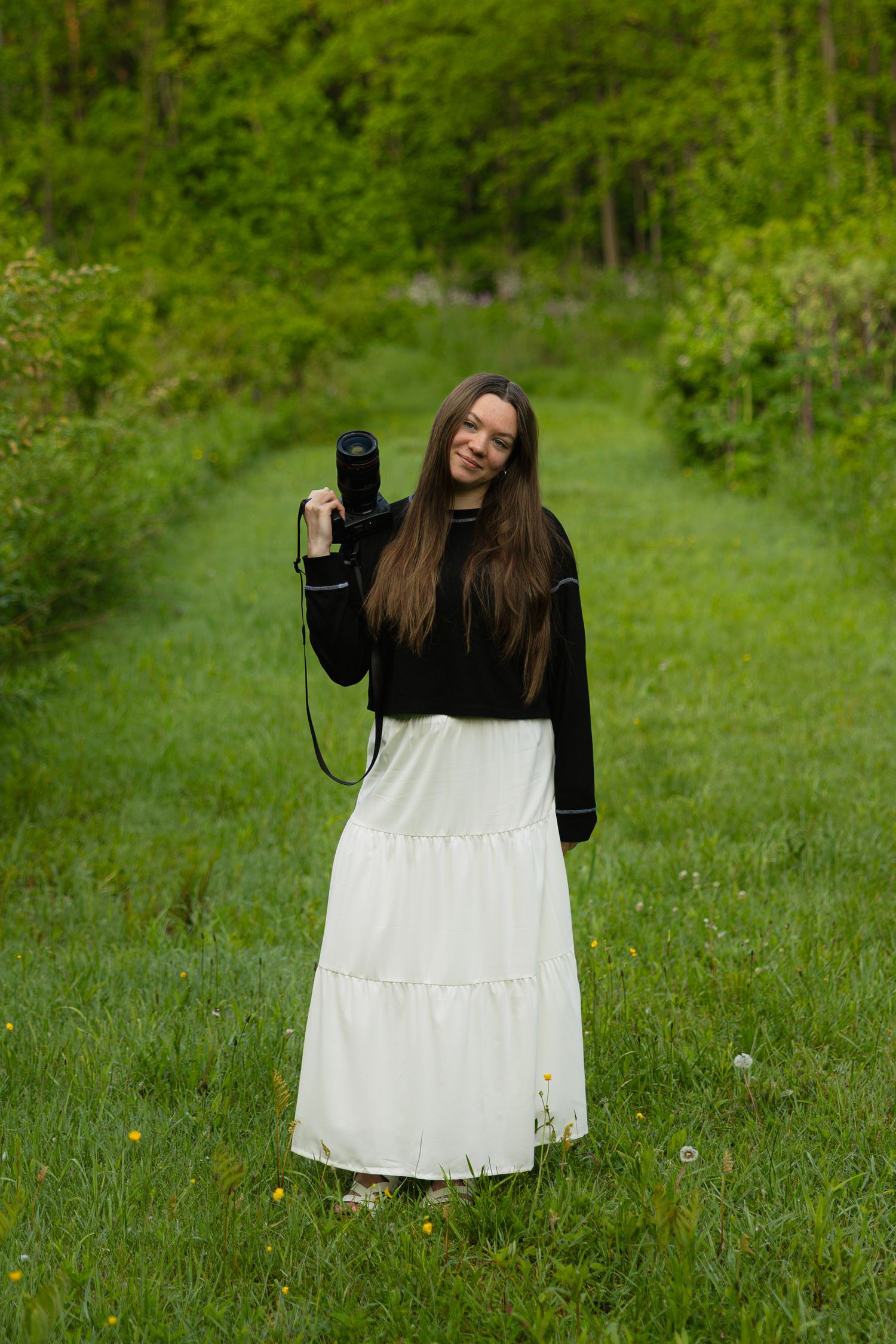 Person holding camera wearing contrasting black and white outfit in verdant garden setting.