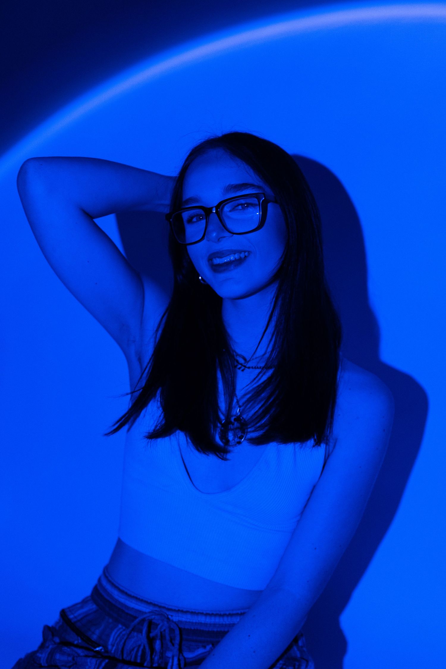 A portrait shot in dramatic blue lighting shows someone wearing glasses and casual attire with a smiling expression.