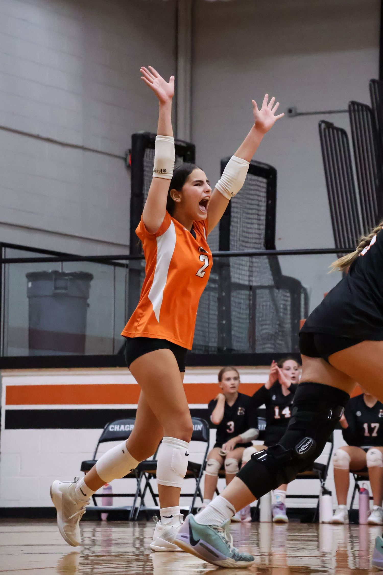 Volleyball players in orange jerseys dive for the ball during indoor match.