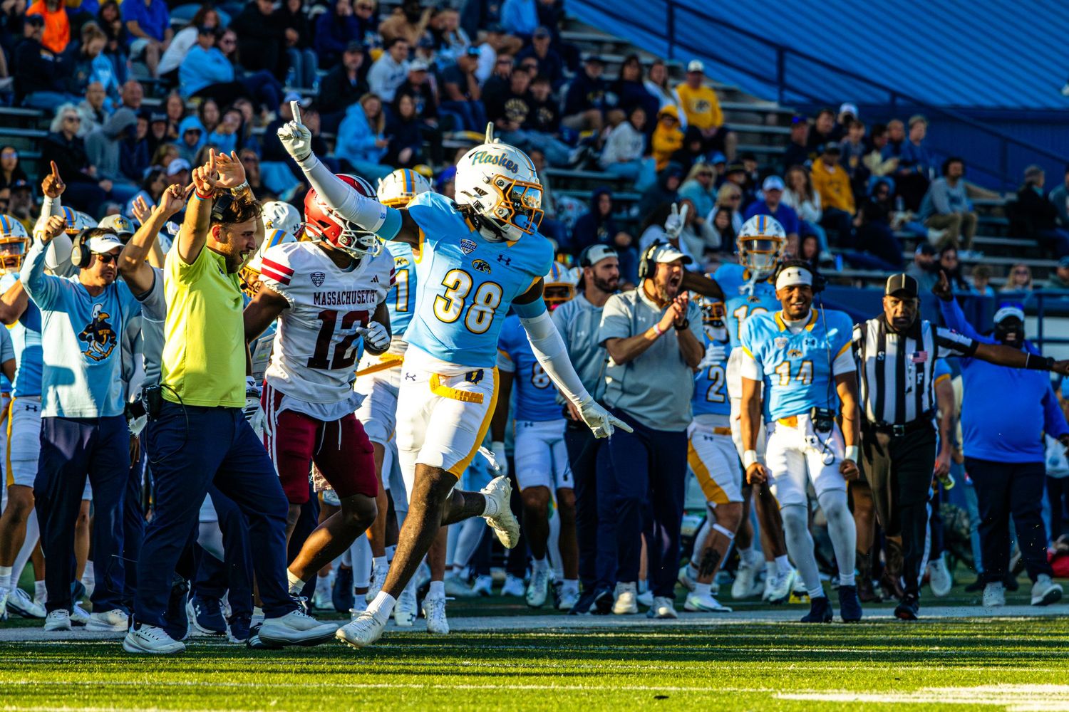 Football players leap and stretch to catch a pass during an intense game play moment at a stadium.