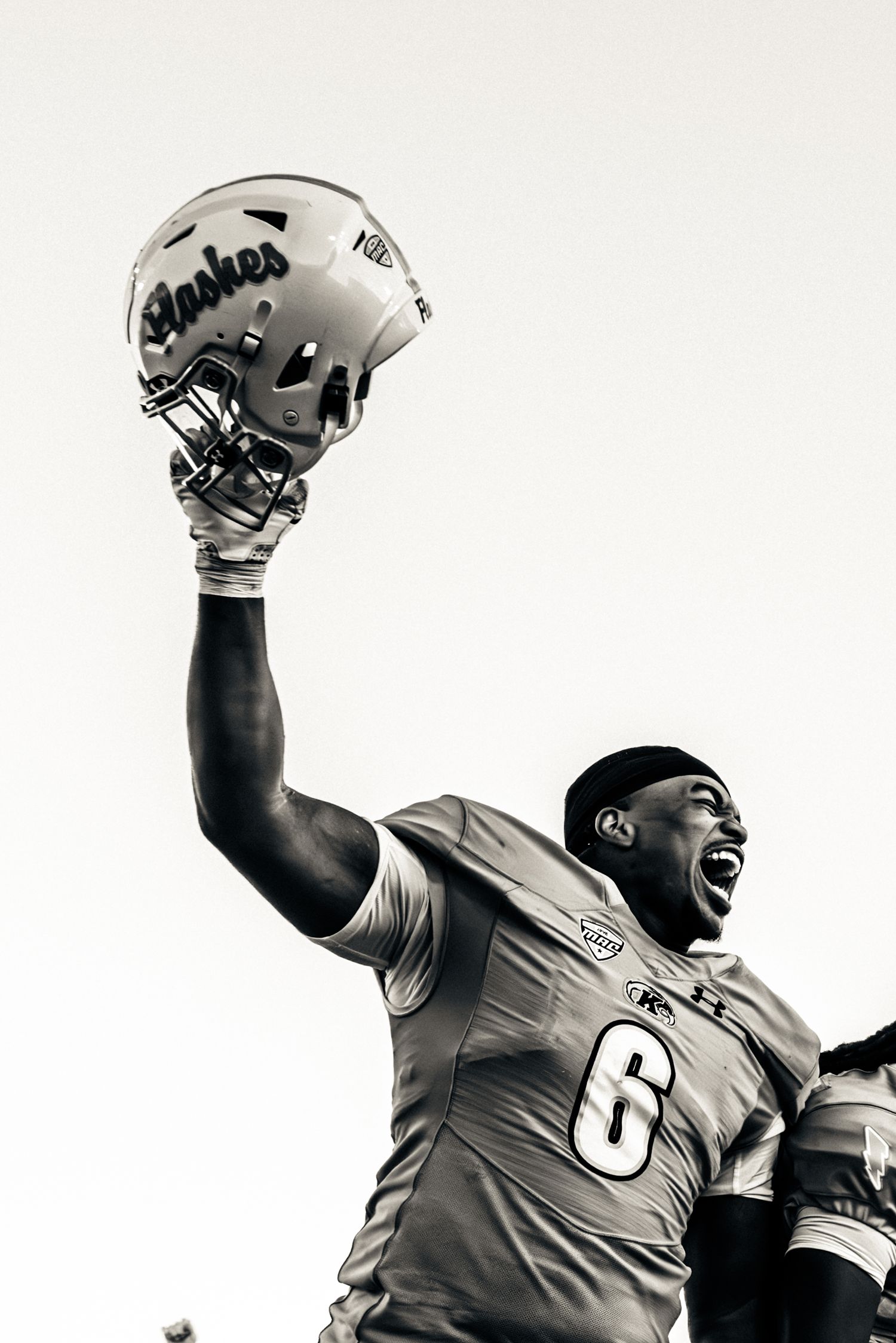 Football players in uniforms celebrate and raise their helmets in a black and white photograph.