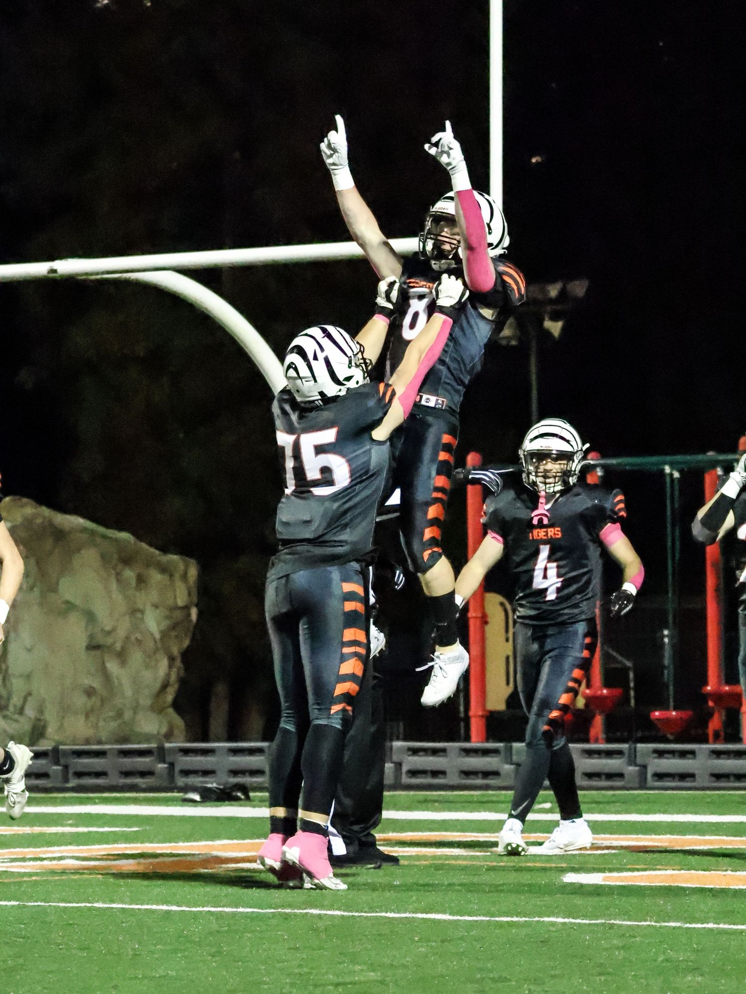 Athletes in black uniforms performing high kicks during a field performance.