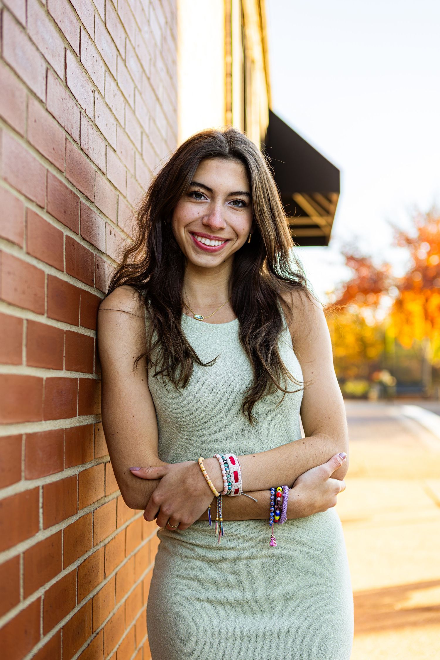 A person wearing a mint green sleeveless top poses against a brick wall during golden hour sunset.