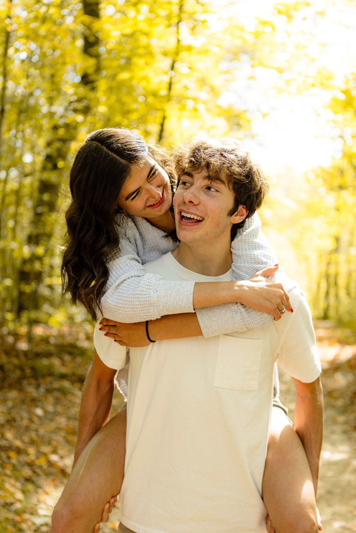 A couple shares a tender moment outdoors on a sunny autumn day with golden yellow leaves in the background.