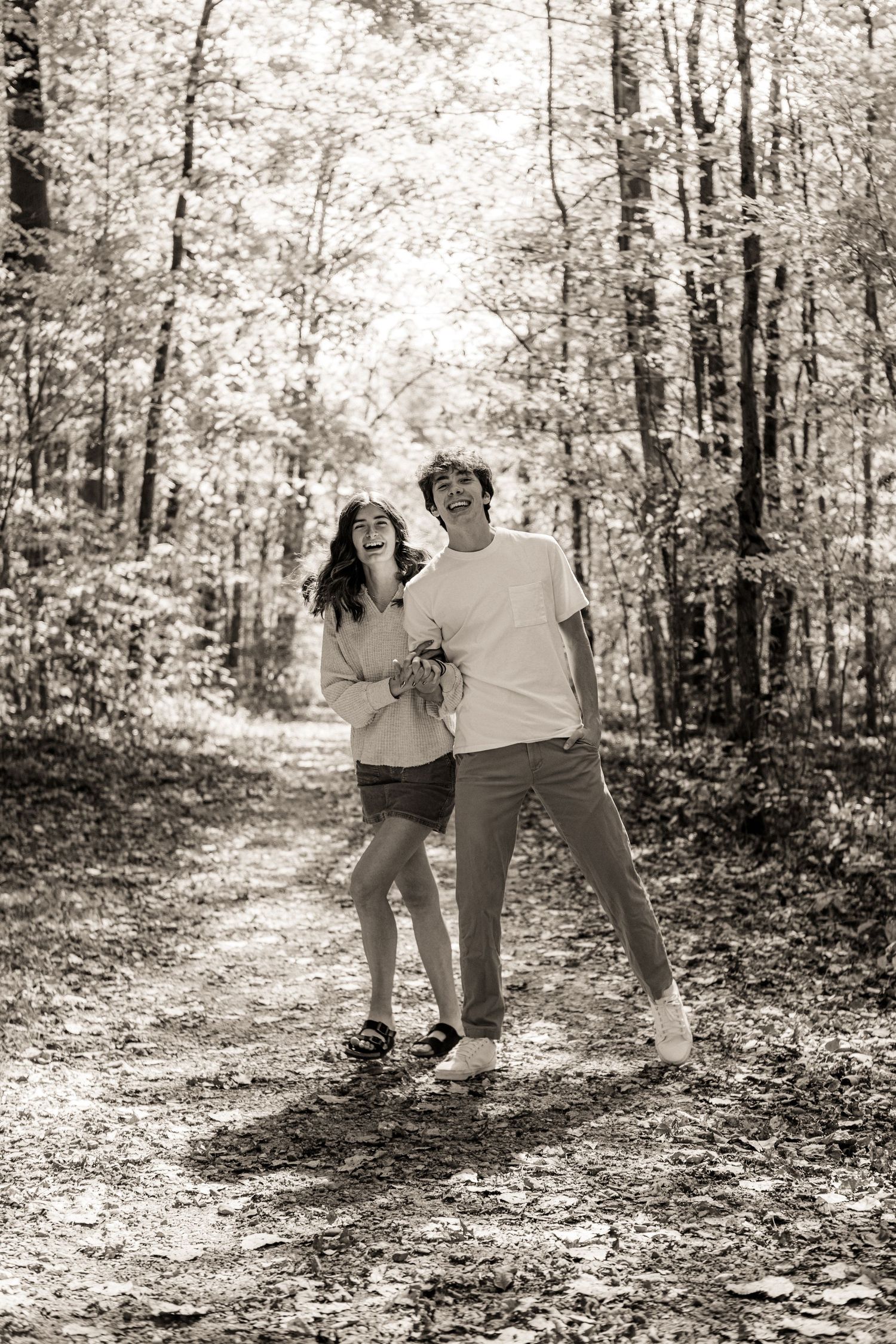 Black and white photo series showing a couple walking and playing together on a leaf-covered forest trail.