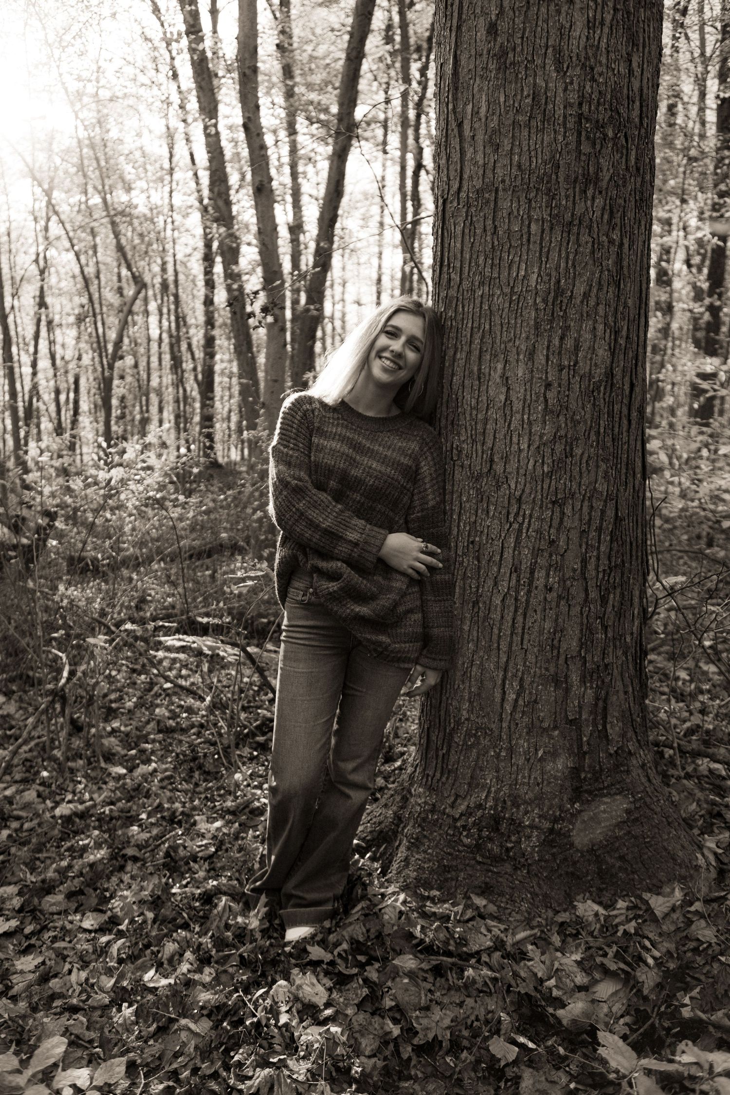 A series of black and white photos showing someone playfully posing and hugging a large tree trunk in the woods.