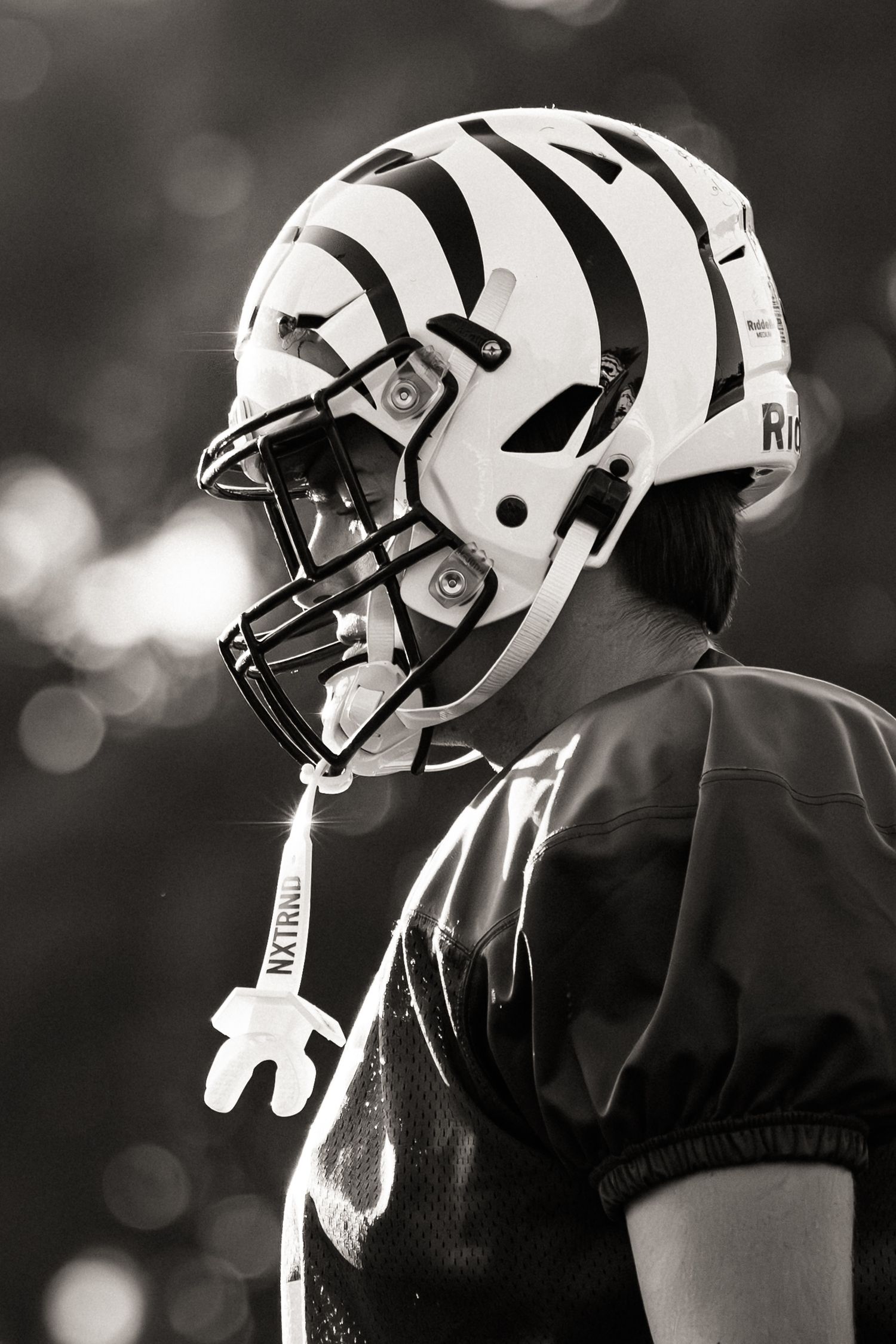 Side profile of football player wearing white helmet with contrasting dark jersey during game practice or competition.
