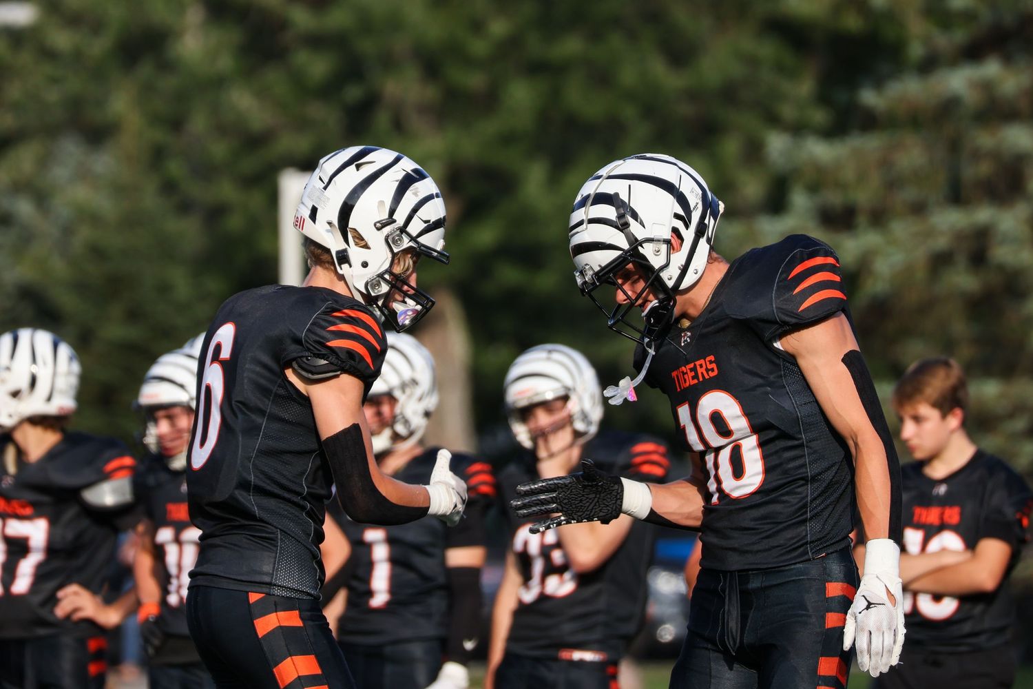Football players in black uniforms with white helmets celebrate on the sideline.