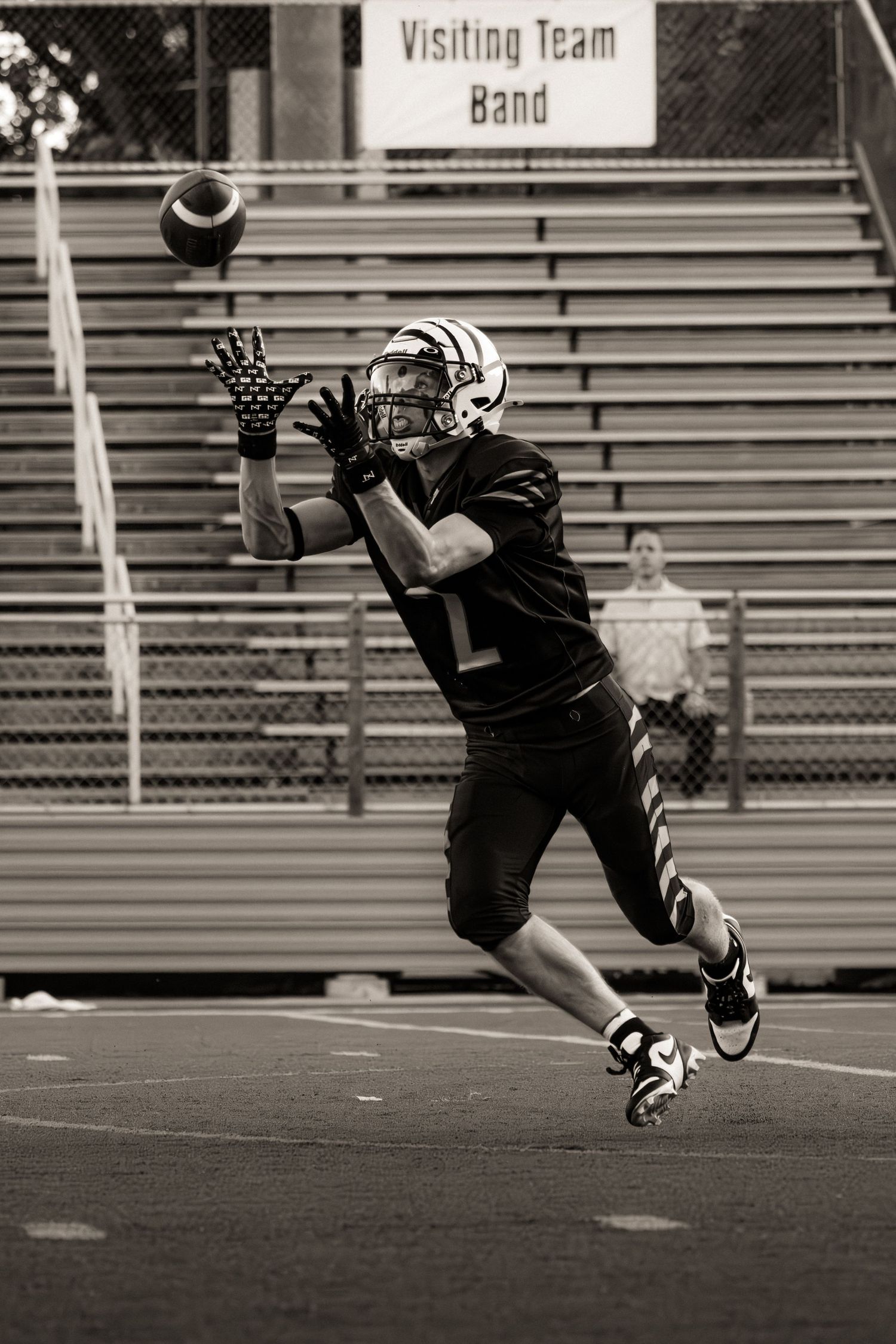 Football player in action demonstrates diving catch sequence in a black and white photograph on empty field.