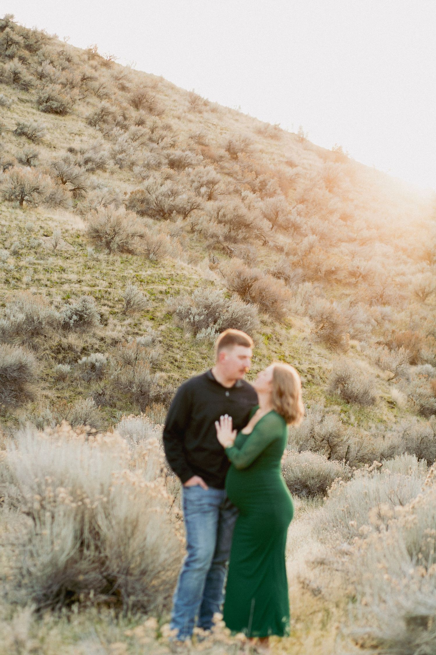 Couple sharing a romantic moment in a sunlit desert landscape, woman in green dress touching man's chest.