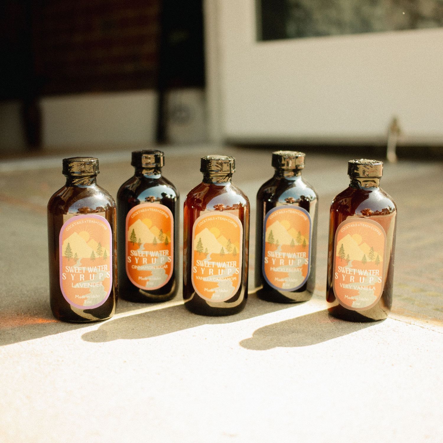 Five amber glass bottles with orange labels arranged in a row on a sunlit surface.