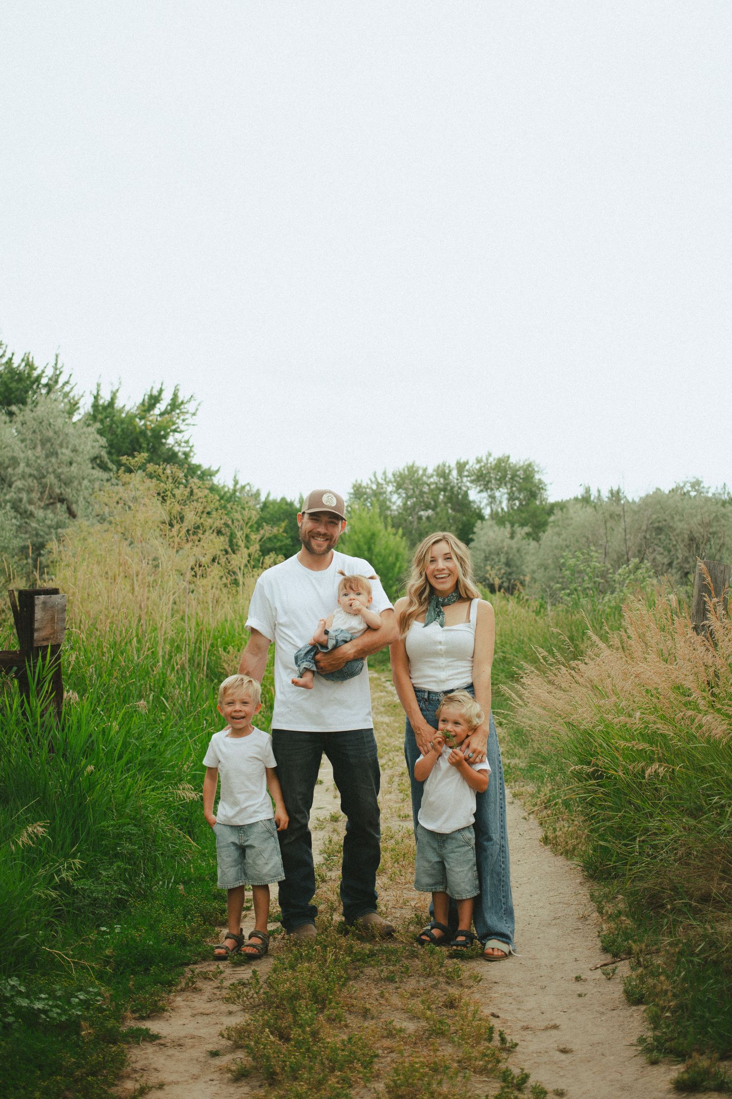 Happy family of five poses on a dirt path surrounded by lush green nature.