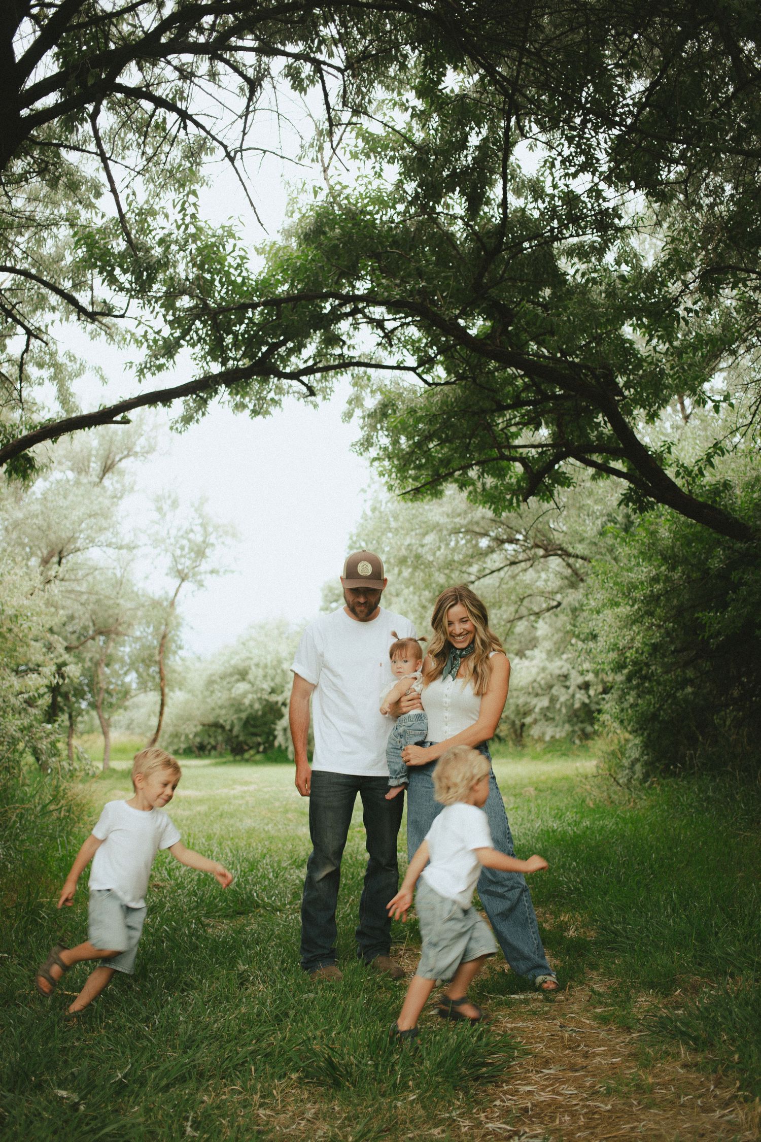 Family of five playing together on a green tree-lined path in nature.