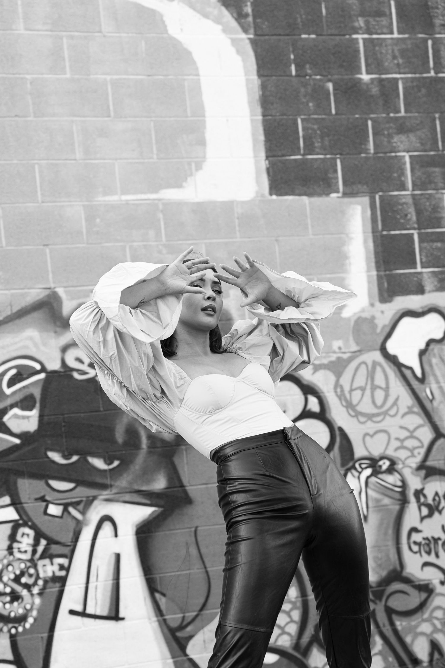 A black and white photo of a model against a graffiti wall, creating dynamic poses and movements.