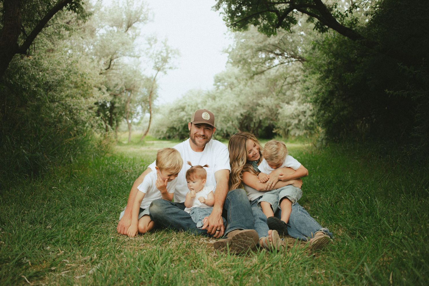 Family of five sitting together on grass in a lush green outdoor setting.