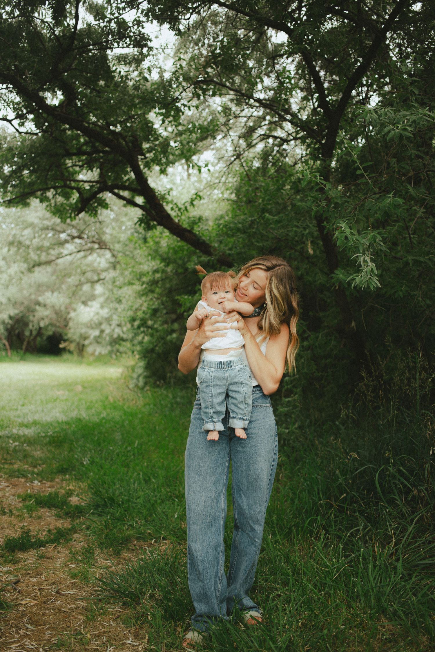 Mother tenderly holding and nuzzling her newborn baby while standing on a green garden path.
