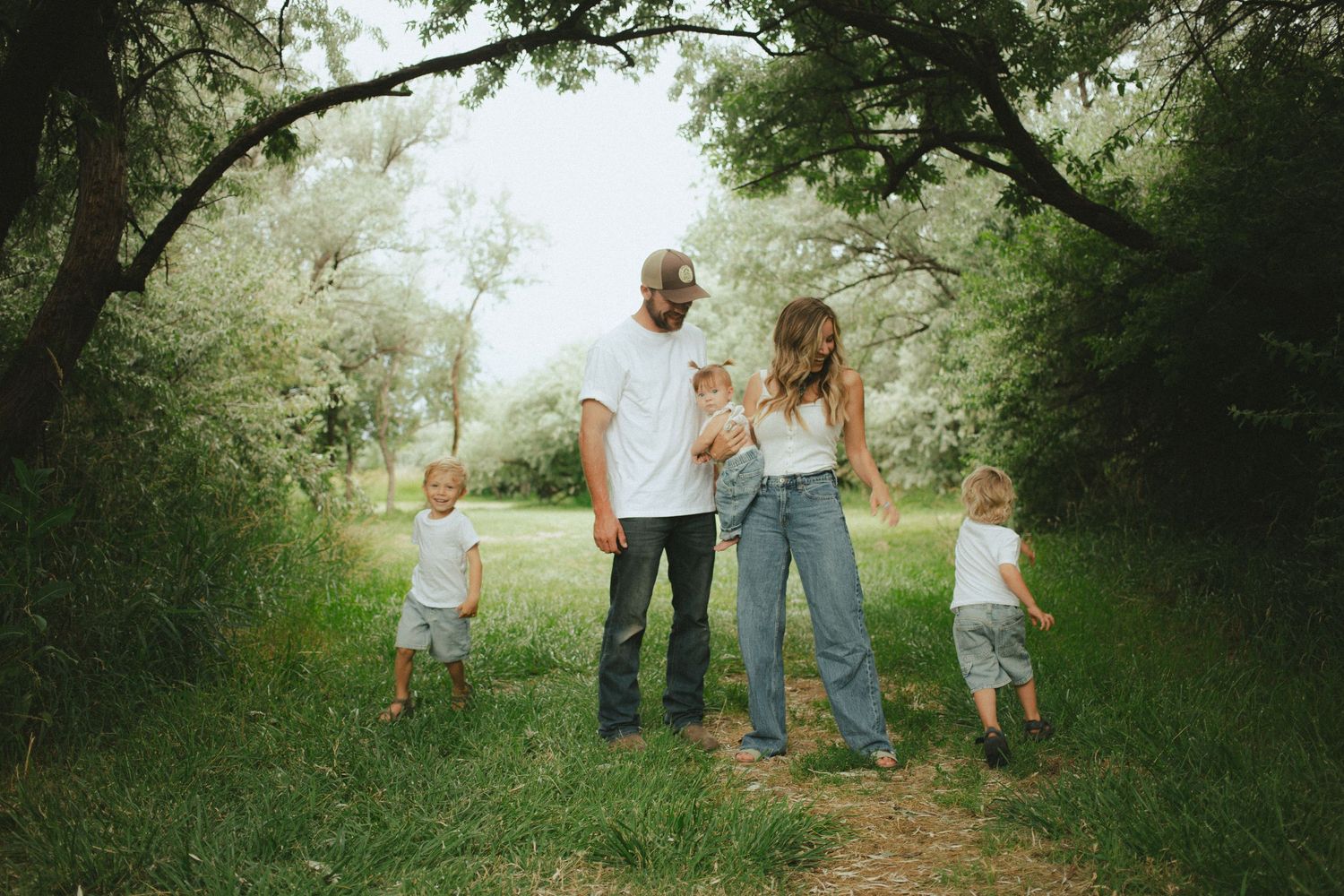 Family of five standing together on a lush green nature trail surrounded by trees.