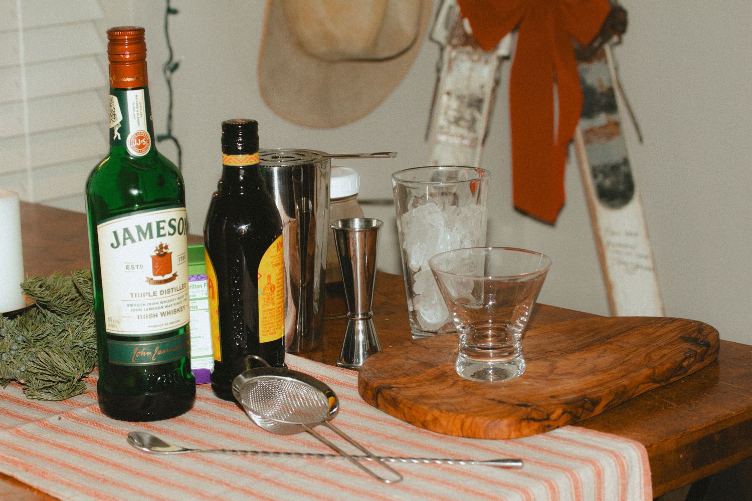 A wooden cutting board with liquor bottles and glassware arranged on a kitchen counter in a cozy house during Christmas time