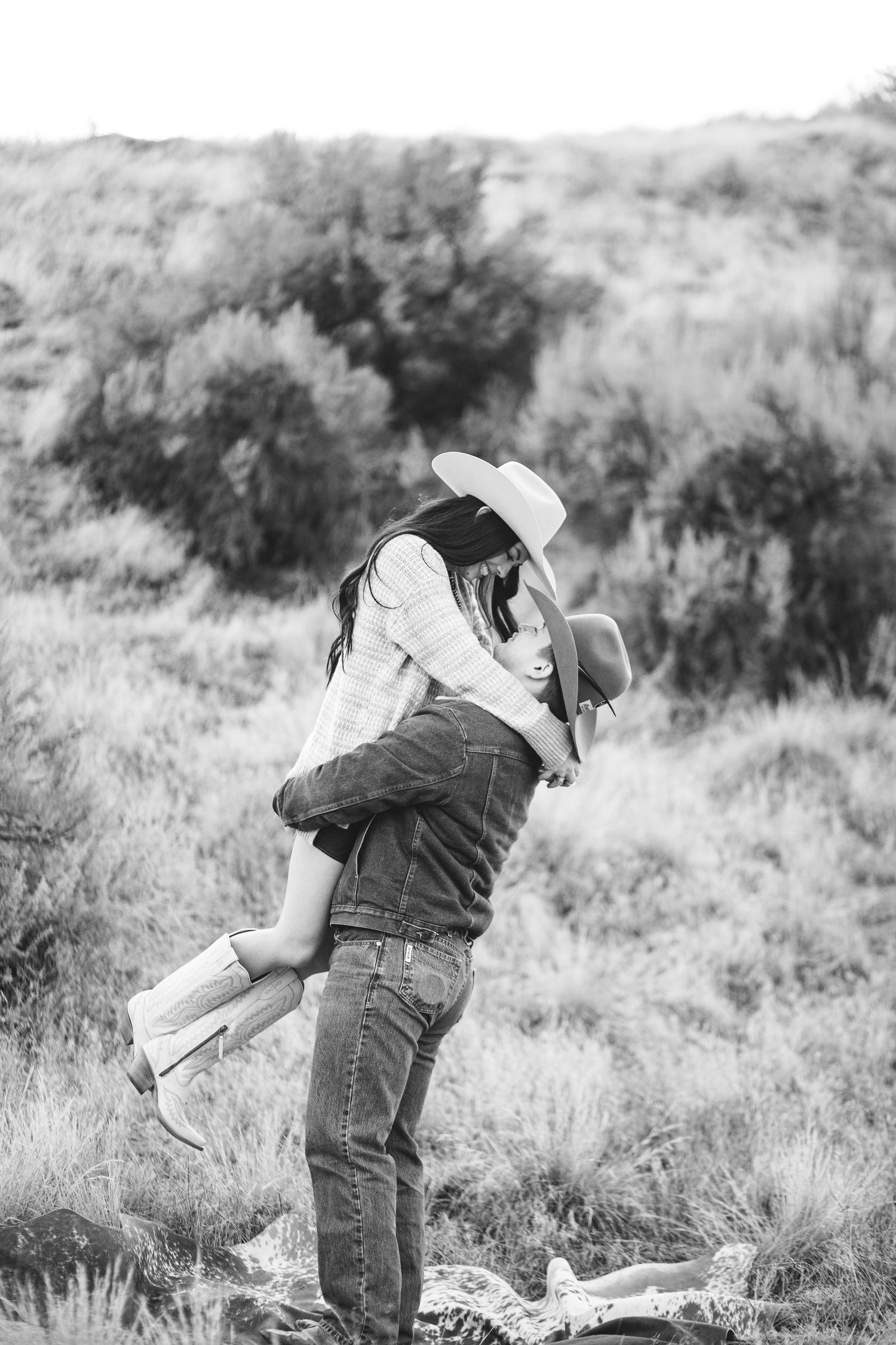 Young man picks up his bride to be in this black and white photo taken in the boise Idaho foot hills.