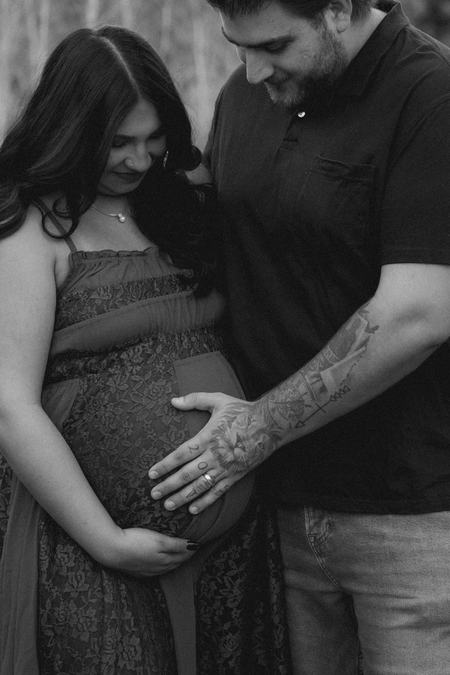 Black and white maternity photo of couple tenderly cradling pregnant belly outdoors.