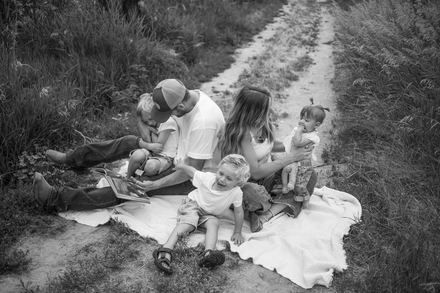 Black and white family photo of parents and children relaxing on a blanket outdoors.