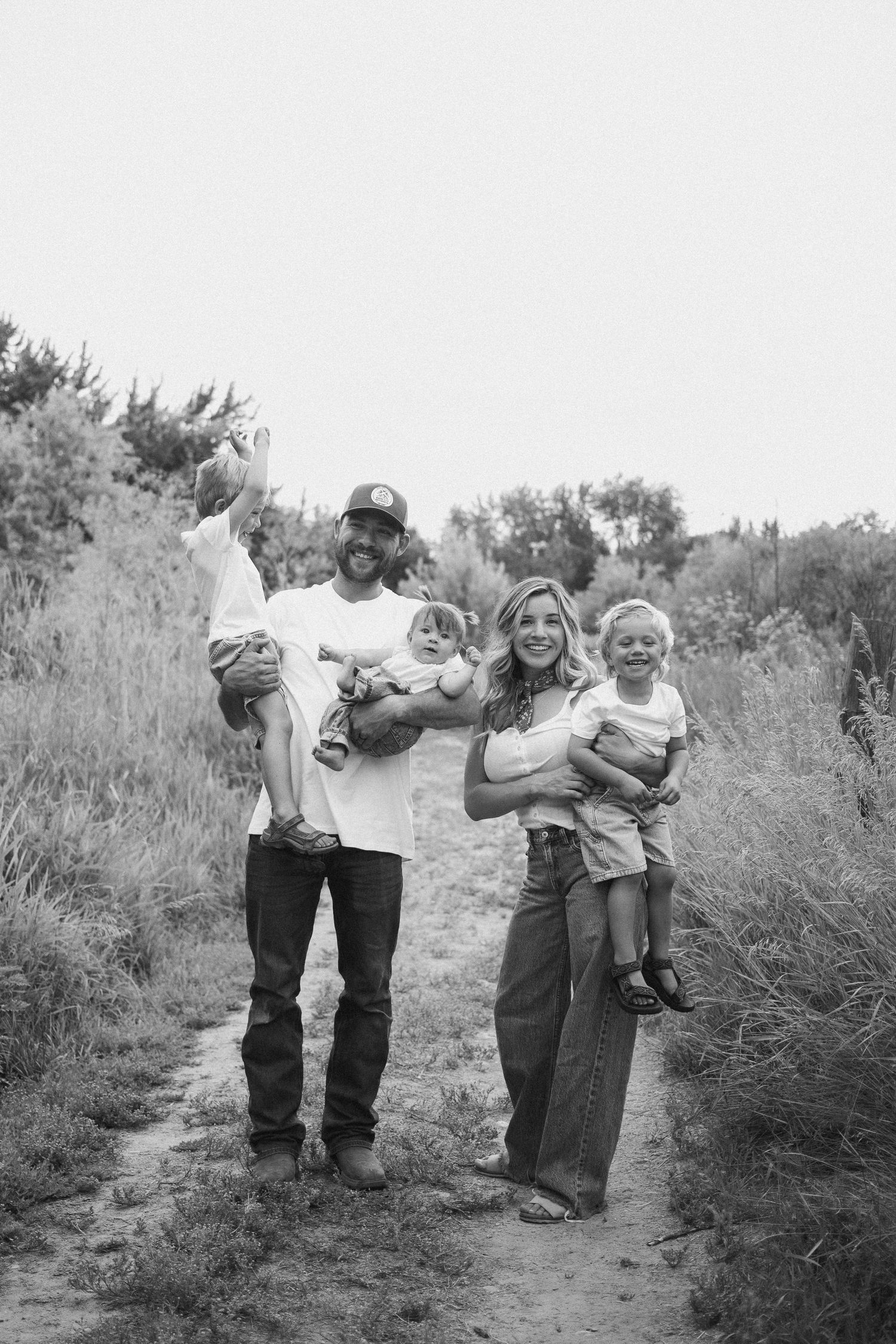 Black and white photo of smiling parents each holding children on a nature trail.