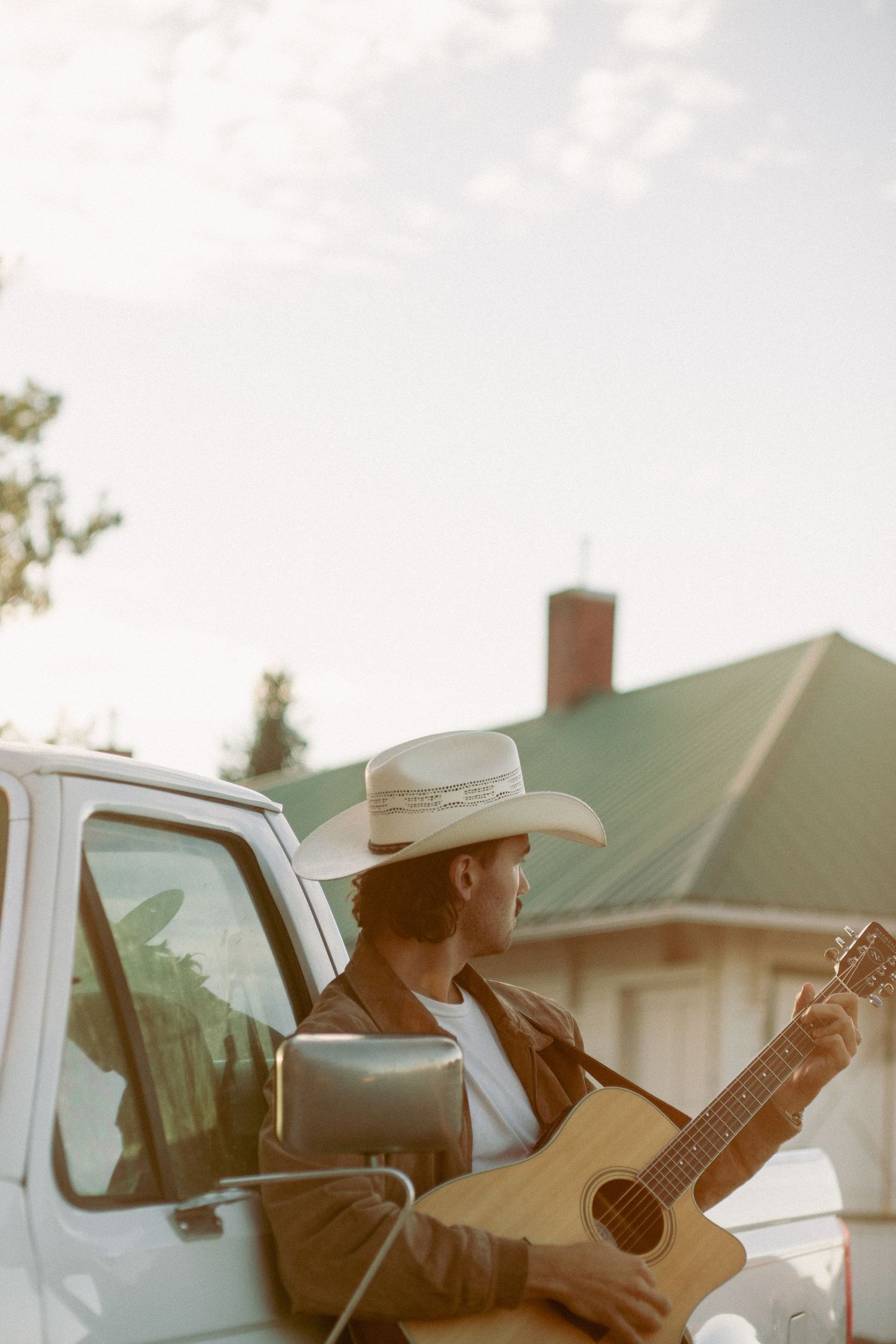 Cowboy plays music on his guitar as he leans against white ford pick up truck in the fresh crisp air in Emmett  Idaho