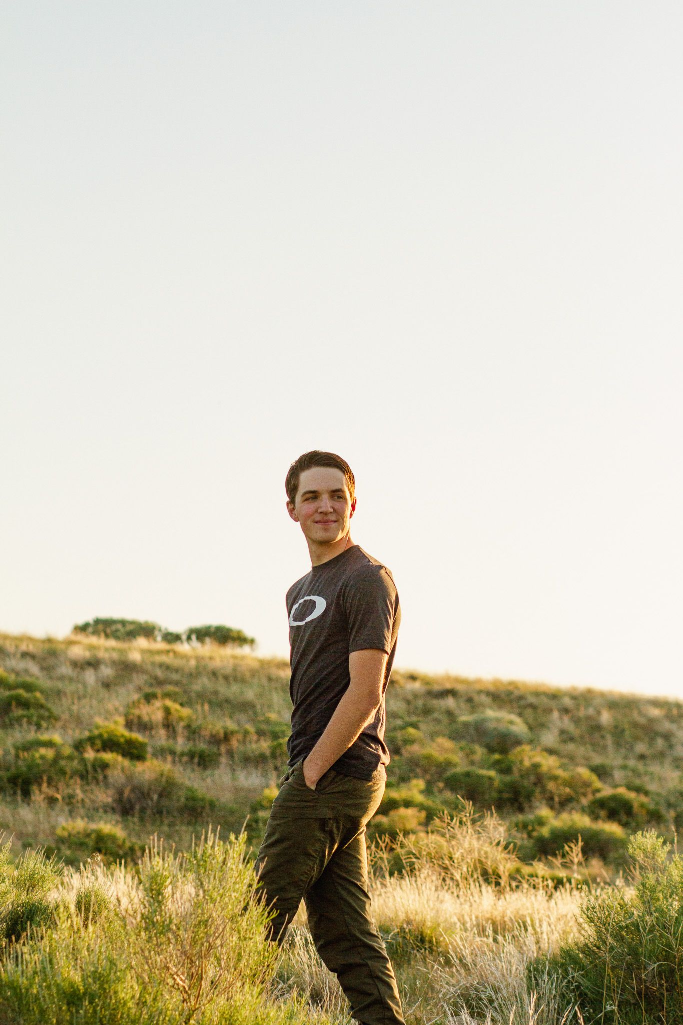 Person in black t-shirt stands in golden sunlit field during sunset with green brush and hills in background located in Boise Idaho