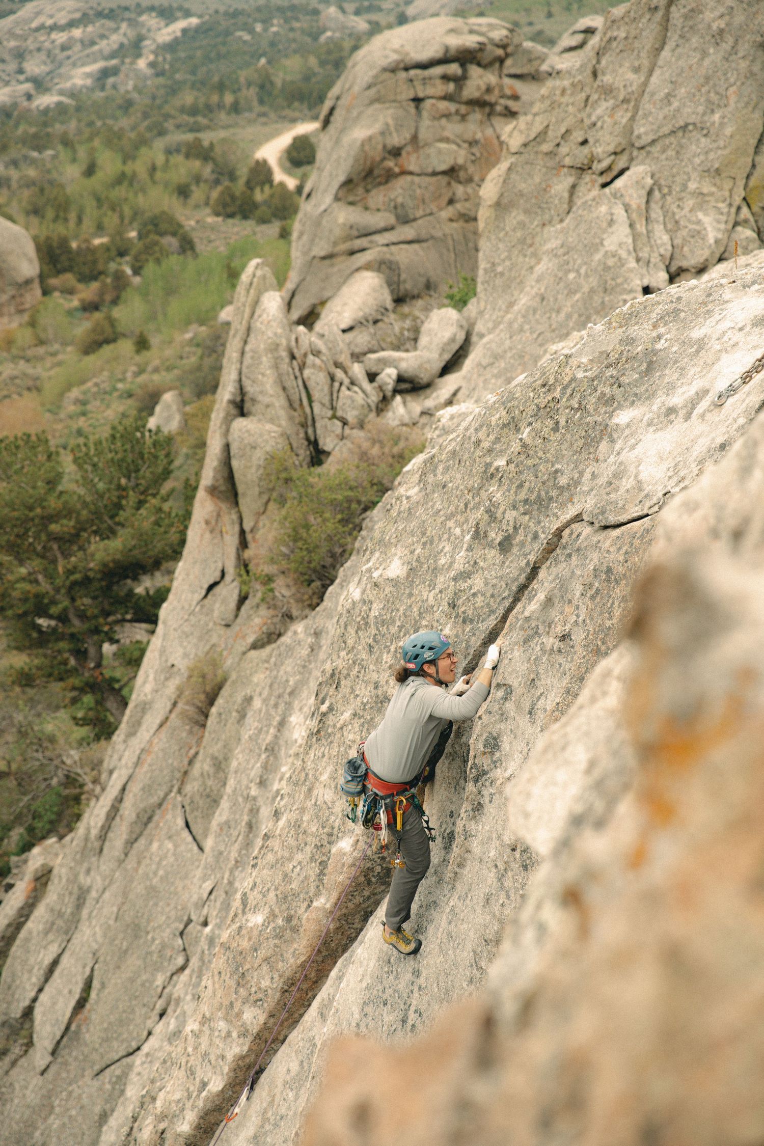Rock climber ascending a steep granite cliff face using technical climbing techniques and safety gear.