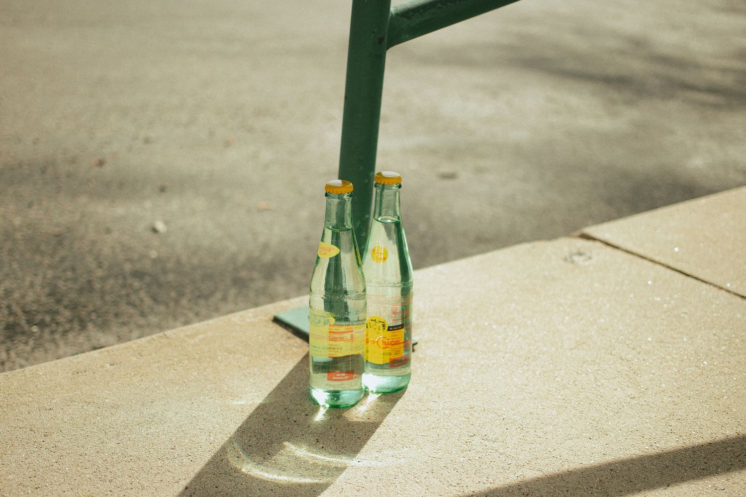 A green glass bottle casts a long shadow on a textured concrete surface in bright sunlight in a hot summer day in Emmett Idaho