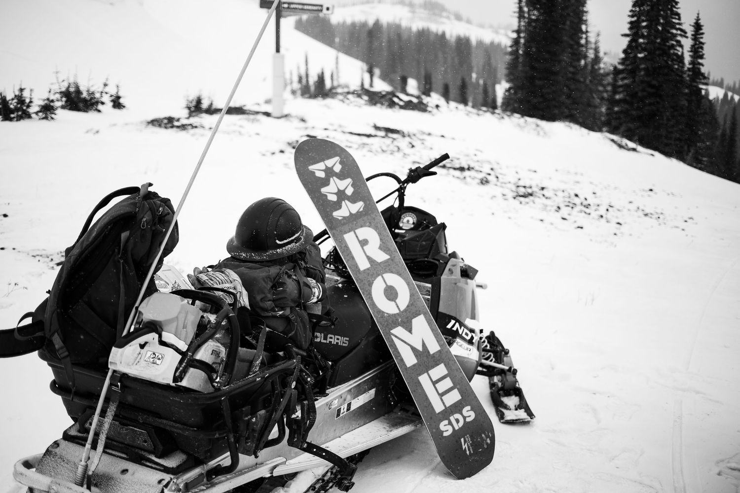 A group of snowmobilers riding through a snowy forest landscape in winter conditions.