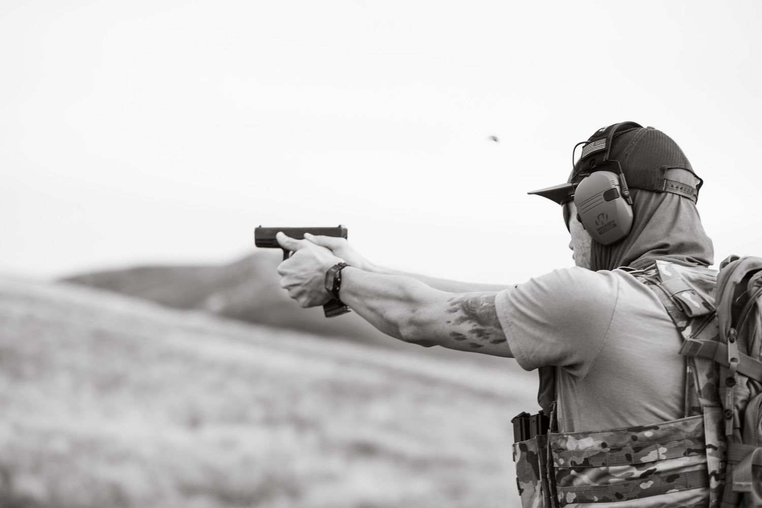 A person aims a handgun while  prone in a shooting position during target practice at an outdoor range.