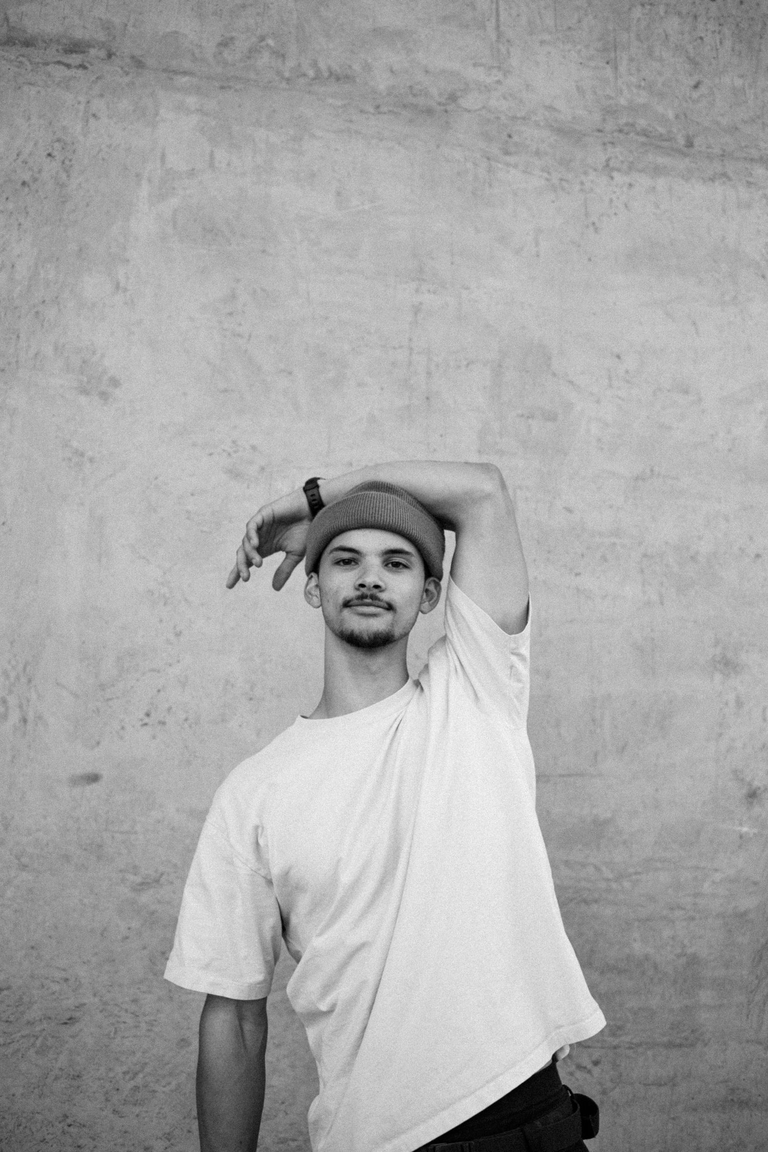 A series of black and white photos showing a person in a white t-shirt making different poses against a concrete wall.