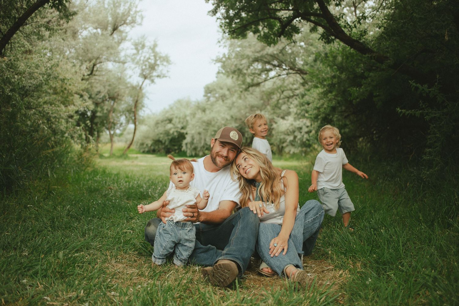 Happy young family with three small children sitting together in a lush green grassy meadow.