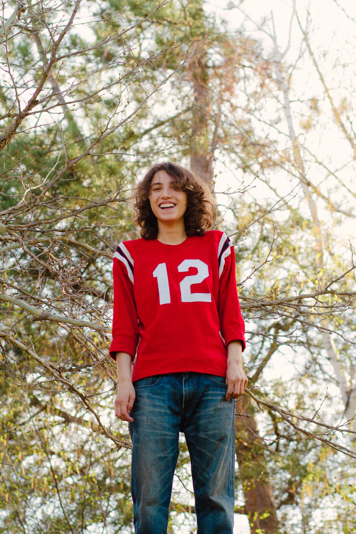 highs cool graduate poses for senior portraits in a lush green setting wearing a red jersey in boise Idaho