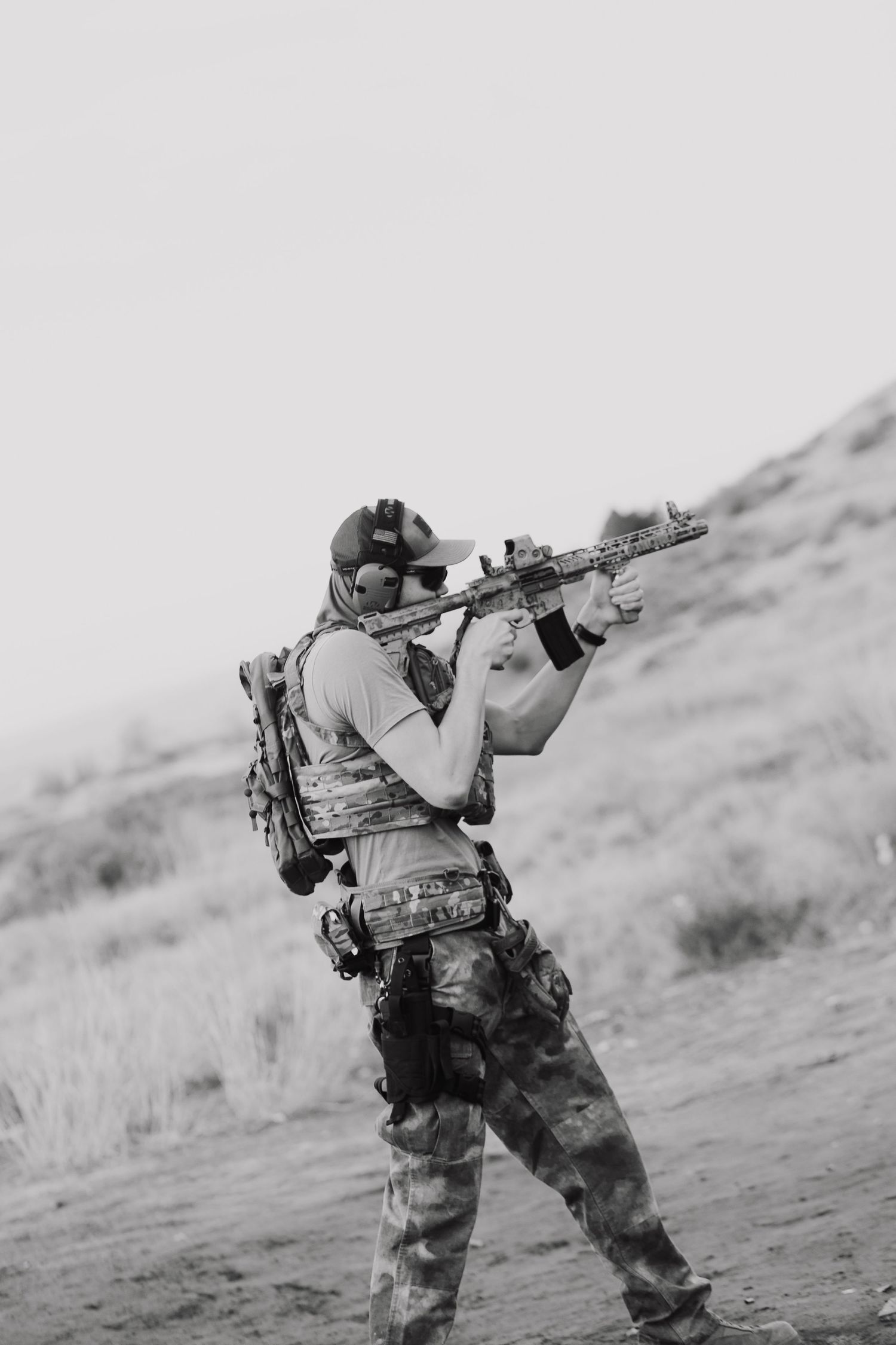 A  black and white photo shows a tactical shooter in camouflage gear taking aim with a rifle in the boise foot hills