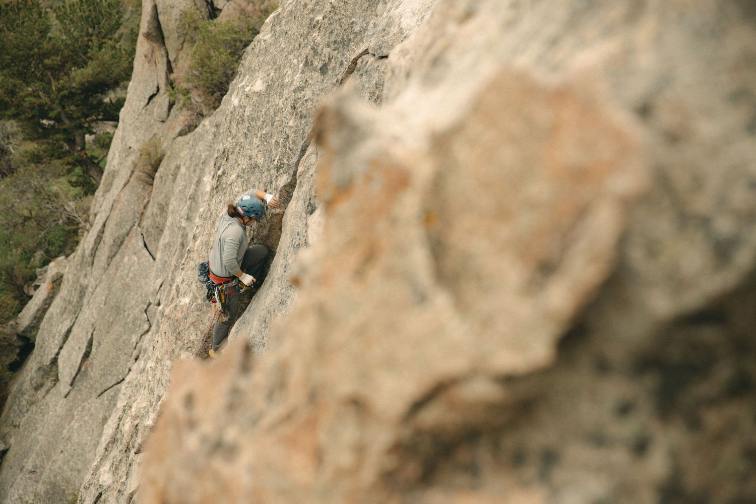 Rock climber scaling a steep limestone cliff face using ropes and climbing gear for protection.