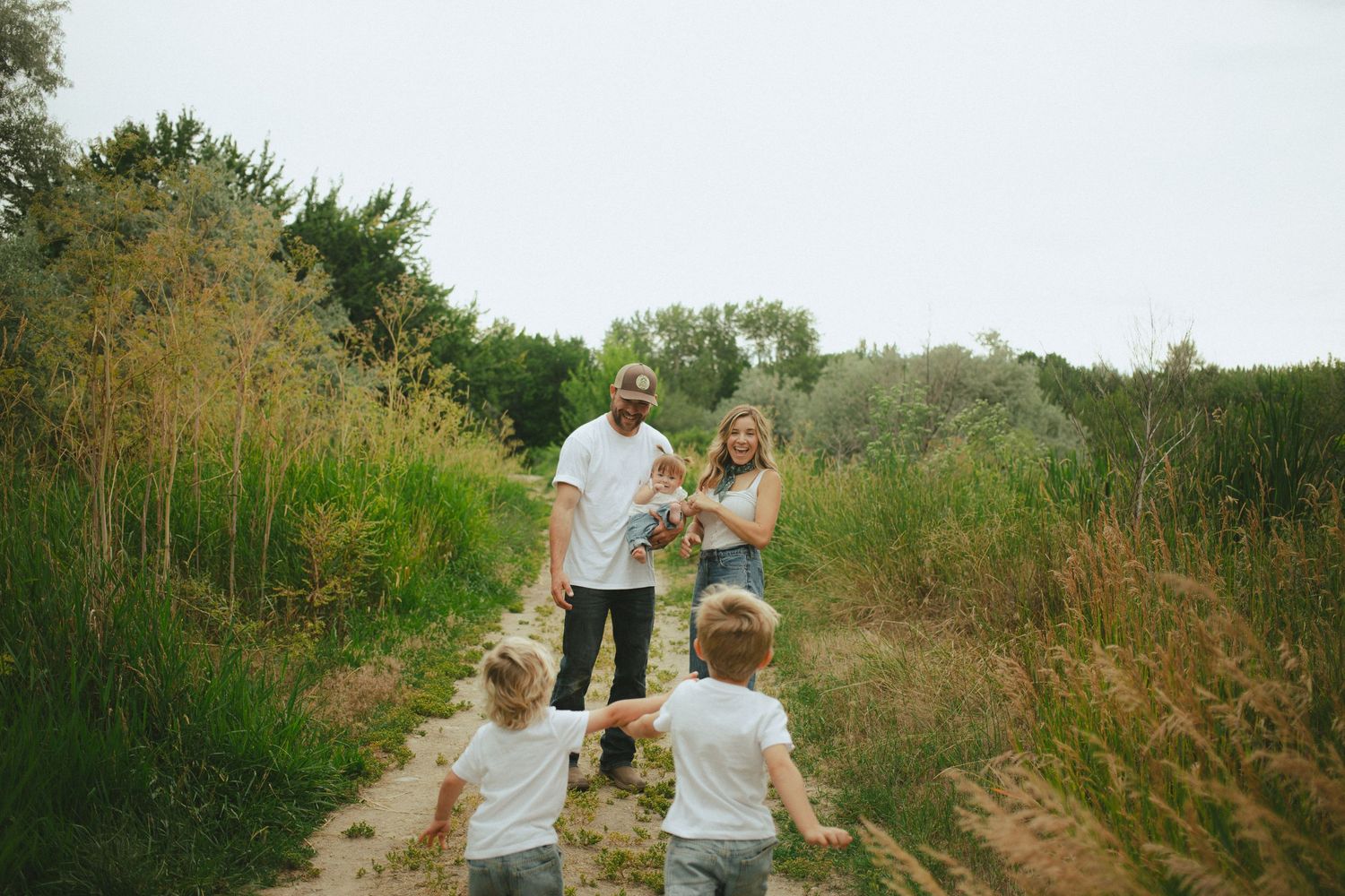Two young children run toward their parents on a scenic outdoor nature trail.