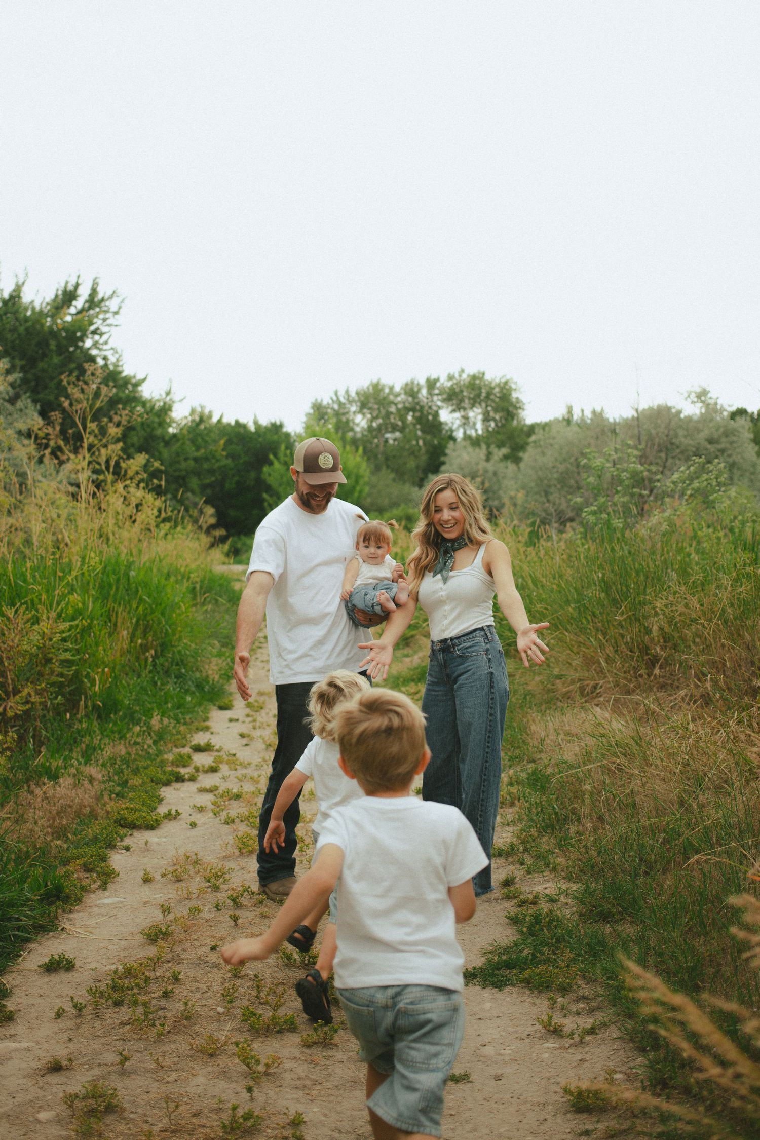 Young boy runs toward his parents holding a baby on a green nature trail.