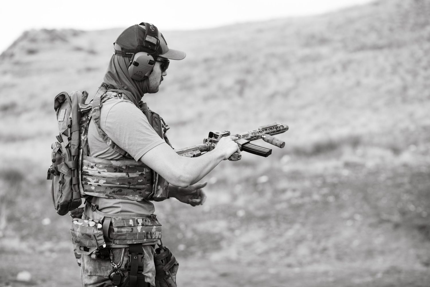 Military personnel in tactical gear practices firearm handling during outdoor training exercise in desert terrain.