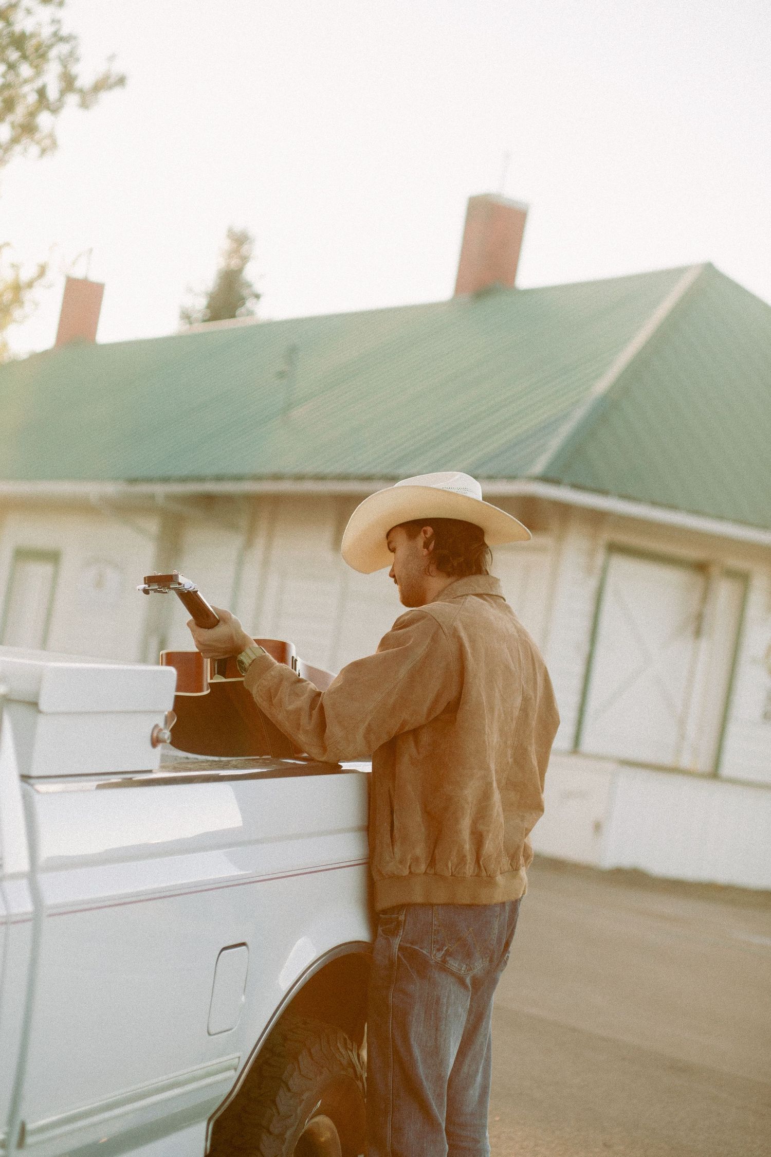 Young man pulls his guitar out of the bed of his white ford pickup getting ready to play music in Emmett Idaho