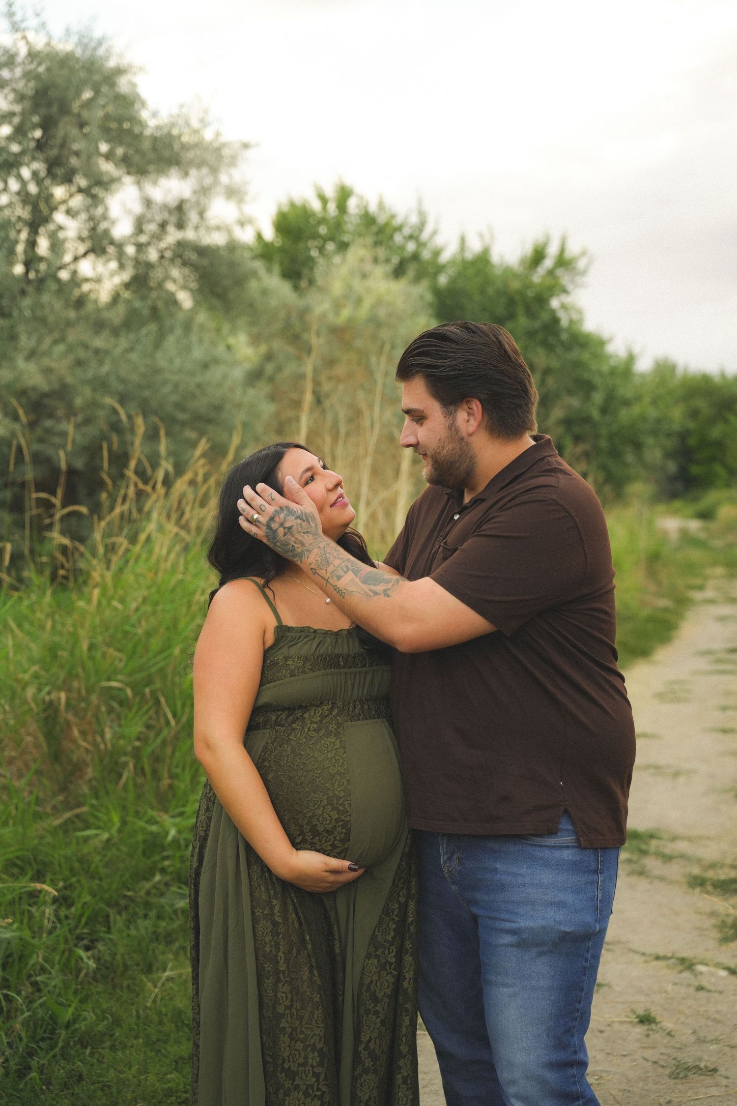Couple sharing a tender moment outdoors, pregnant woman in green dress cradling her belly while partner gently touches her face.